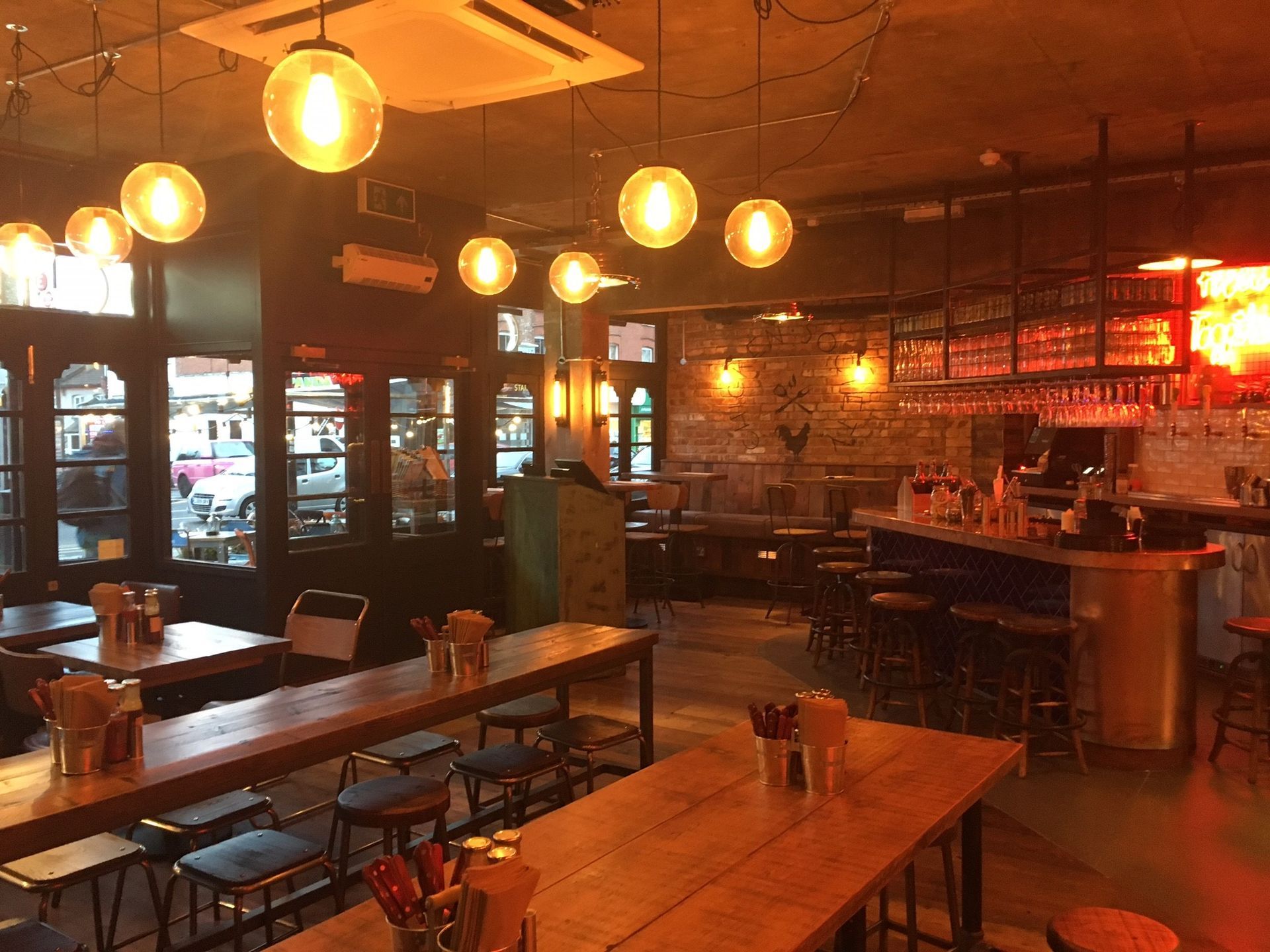 Chicken Society, Finchley, London, view towards main entrance and bar servery, showing industrial finishes and industrial lighting, wood plank tables, and reclaimed timber flooring.