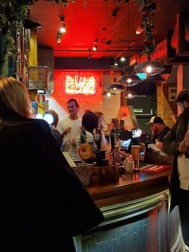 London Road Brew House, Southampton, view along bar counter at night, showing industrial caged feature neon lighting and industrial pendant lights.