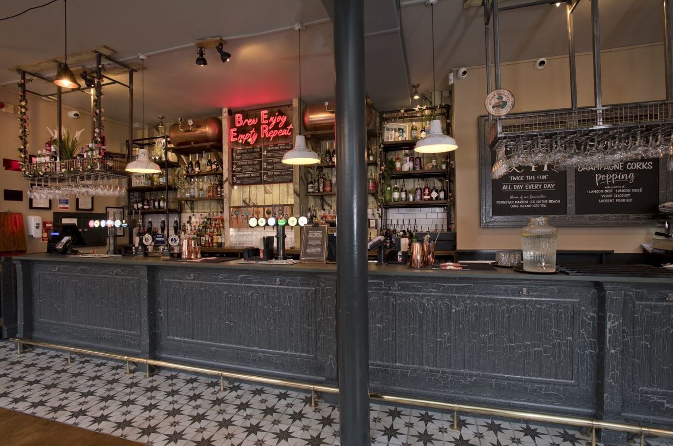 Prince of Teck, Earls Court, London, view of full length of ground floor bar counter with distressed finishes, overbar glassware gantries, and overbar pendants.