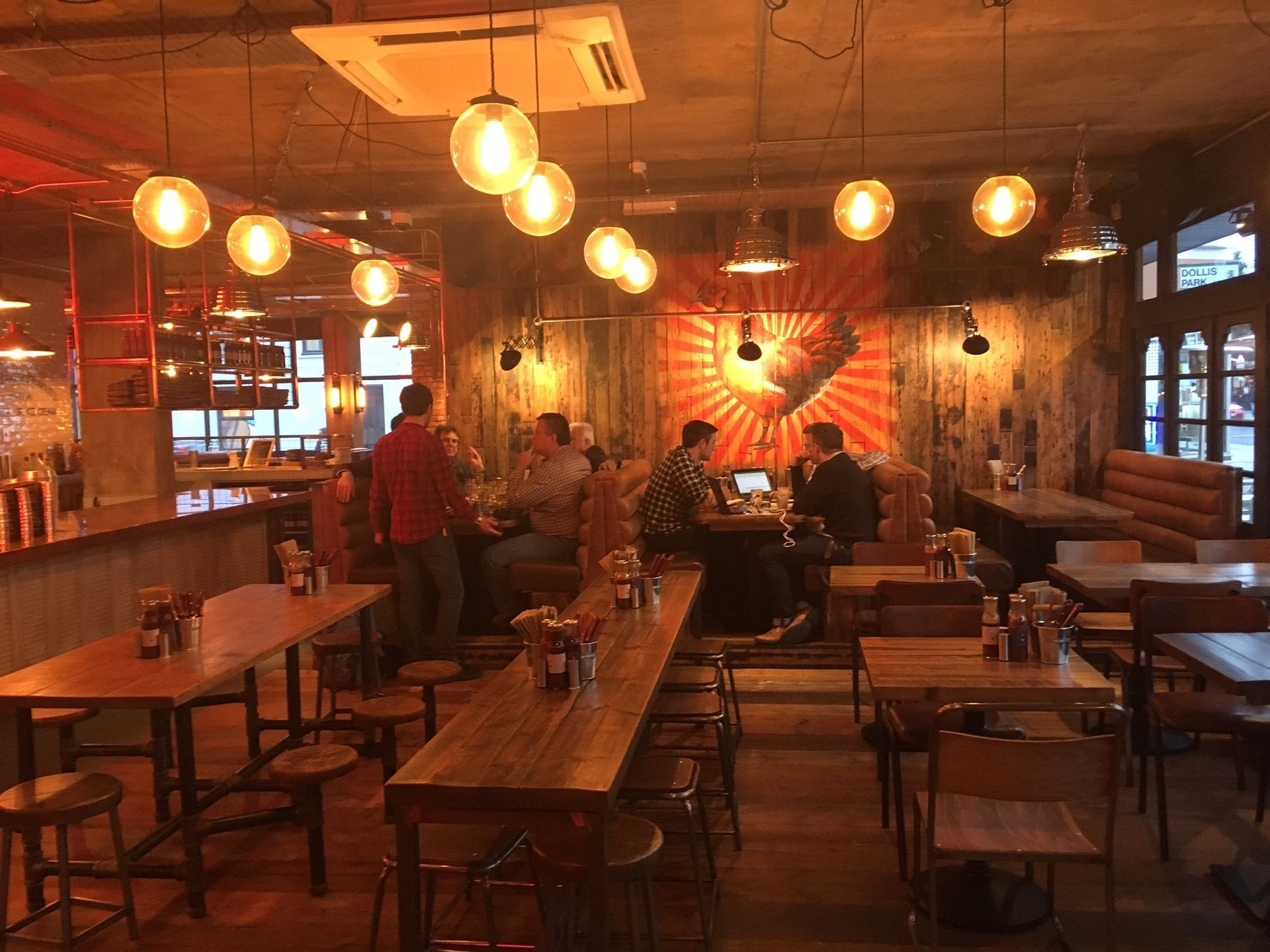 Chicken Society, Finchley, London, view showing central seating area, feature industrial pendant lights, and feature mural to brick wall.