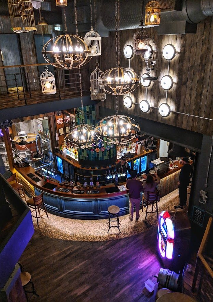 London Road Brew House, Southampton, looking down from first floor to the ground floor bar counter, industrial finishes along with industrial feature wall lighting and bird cage pendants.