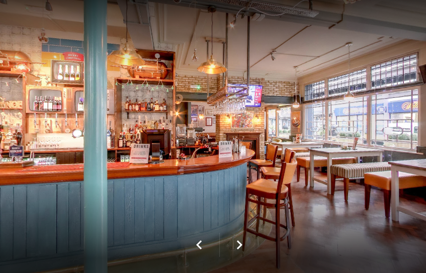 Whitecross Tap, Old Street, London, painted timber panelled bar front, overhead pendant lights and glassware gantry over bar.