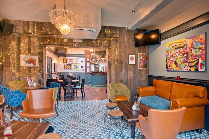Whitecross Tap, Old Street, London, rear ground floor lounge area with sofas and tub chairs, timber clad walls and feature artwork.