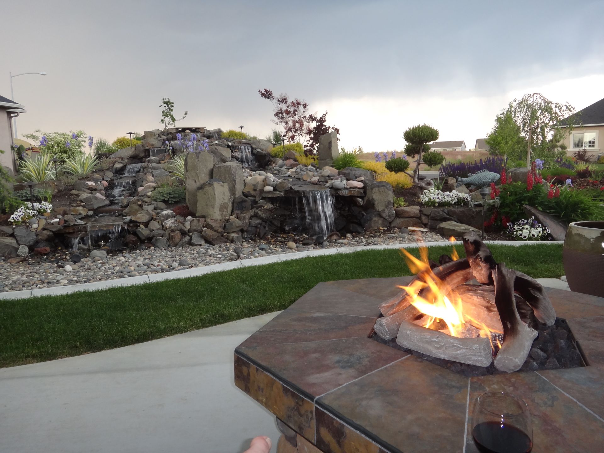 A fire pit in a backyard with a waterfall in the background
