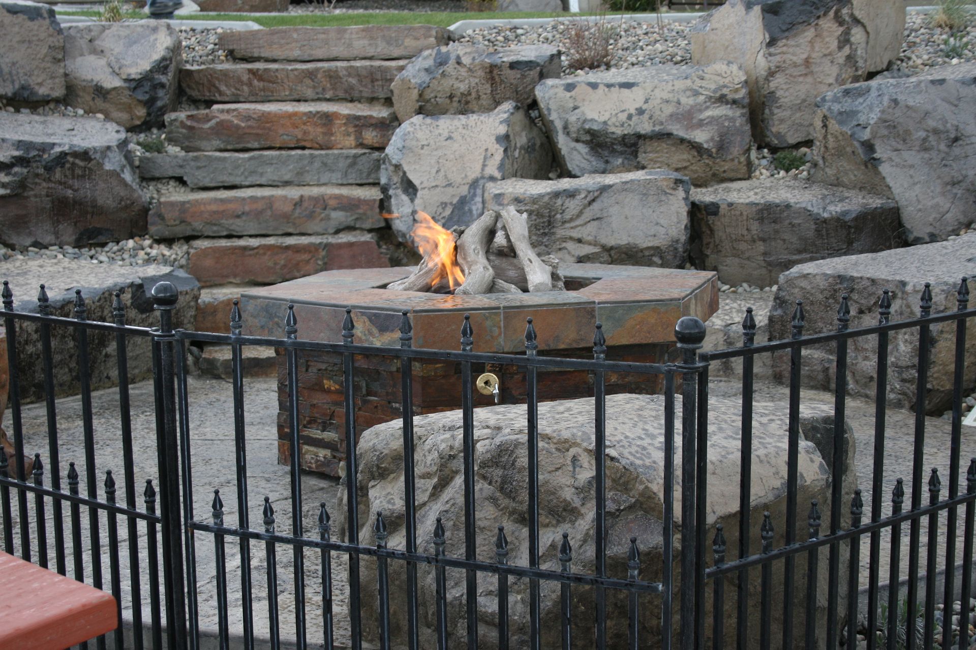 A fire pit is surrounded by a metal fence and rocks.