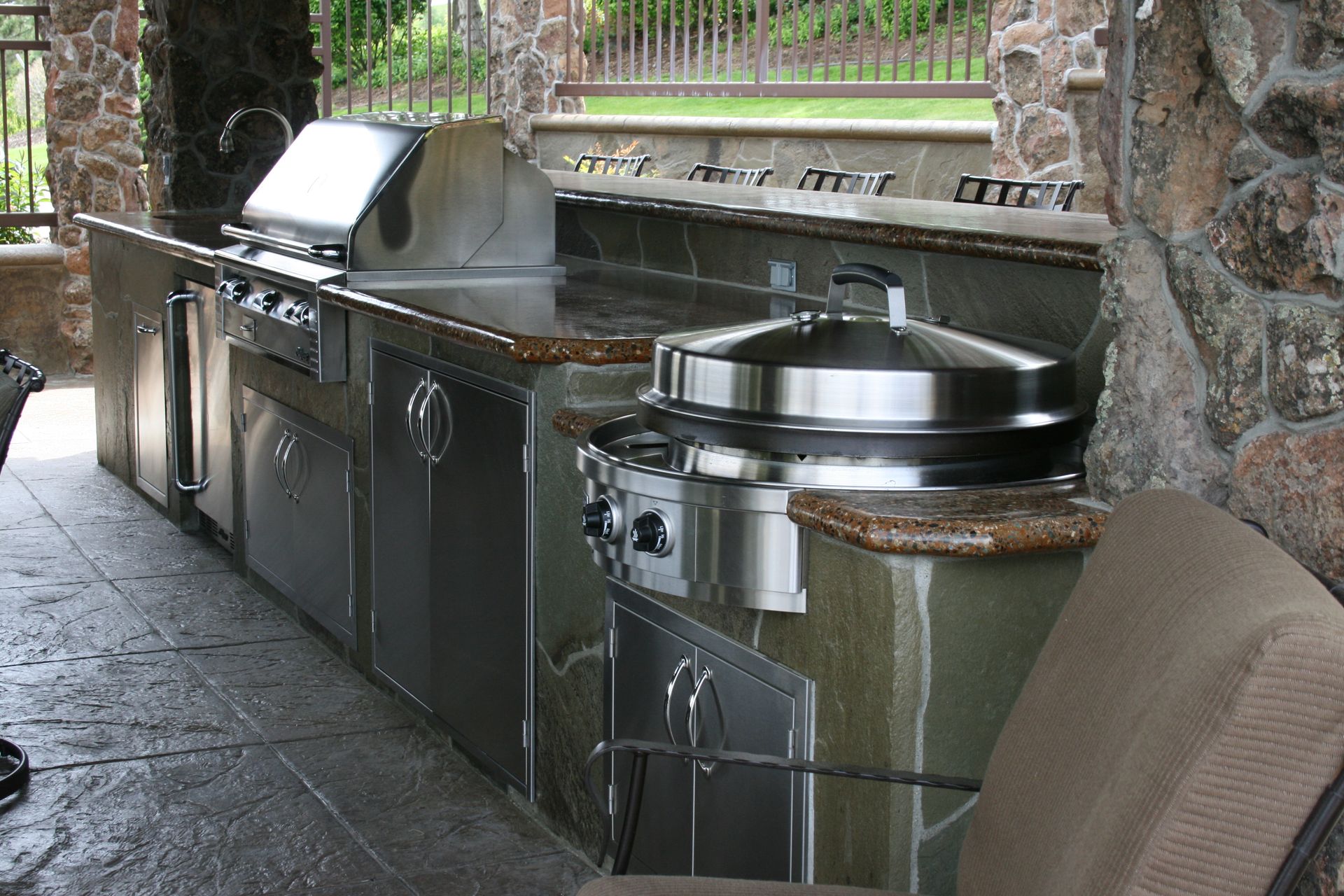 An outdoor kitchen with stainless steel appliances and a chair