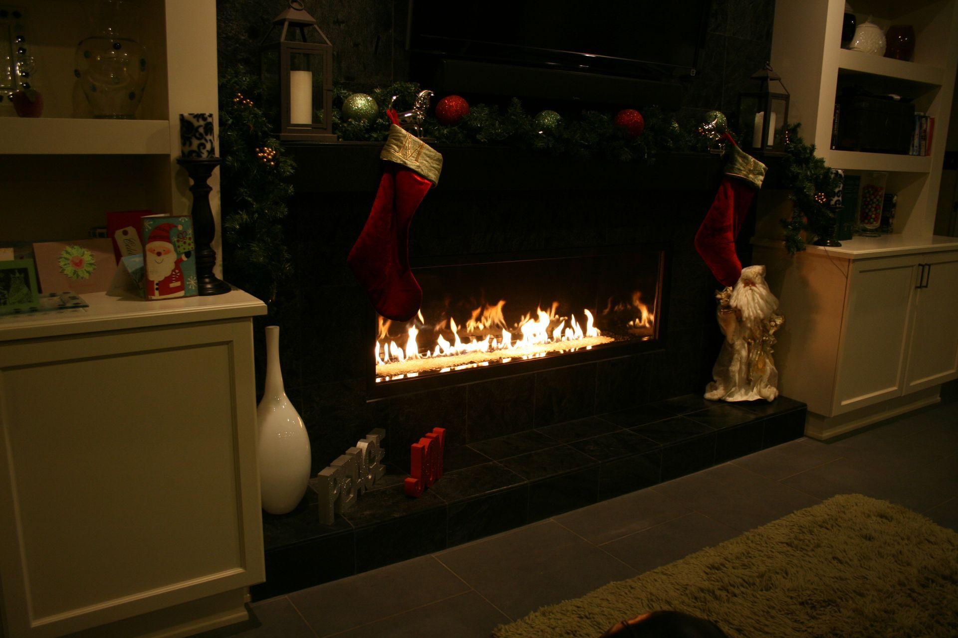 A living room with a fireplace decorated for christmas with stockings on it.