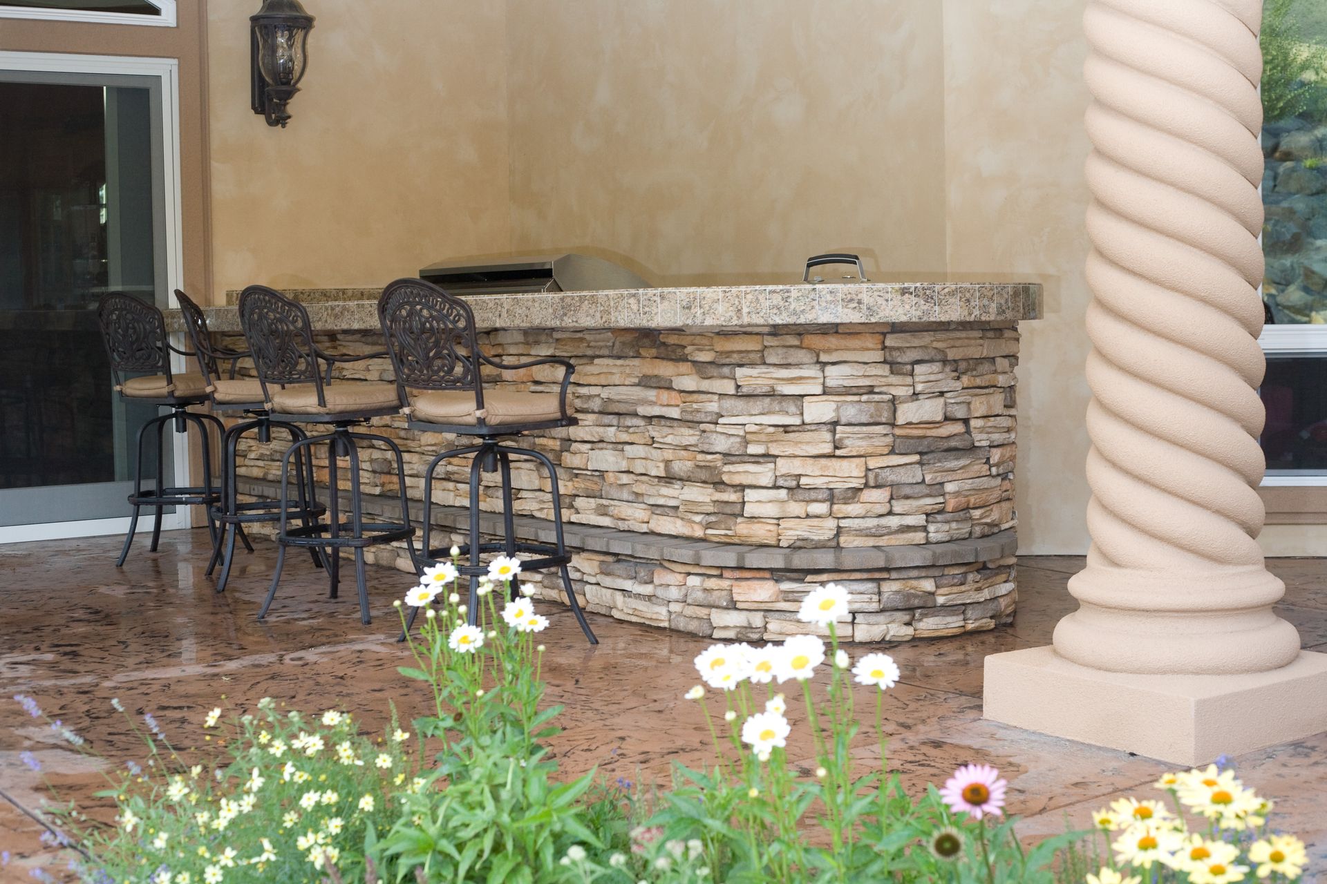 A patio with a stone bar and chairs surrounded by flowers