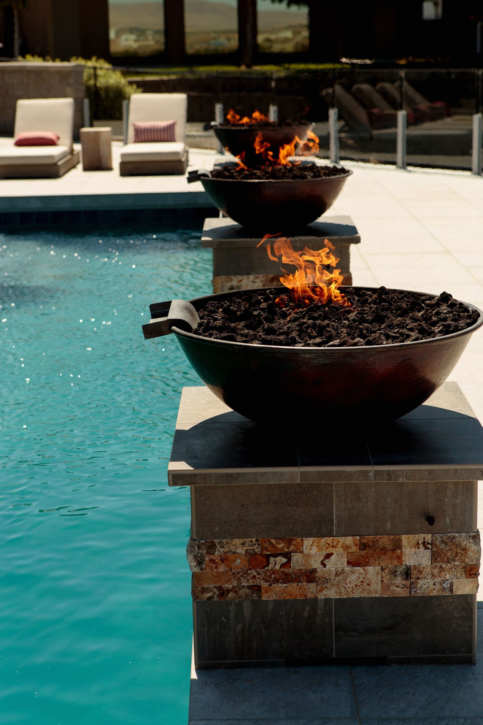 Three bowls of fire are sitting next to a swimming pool