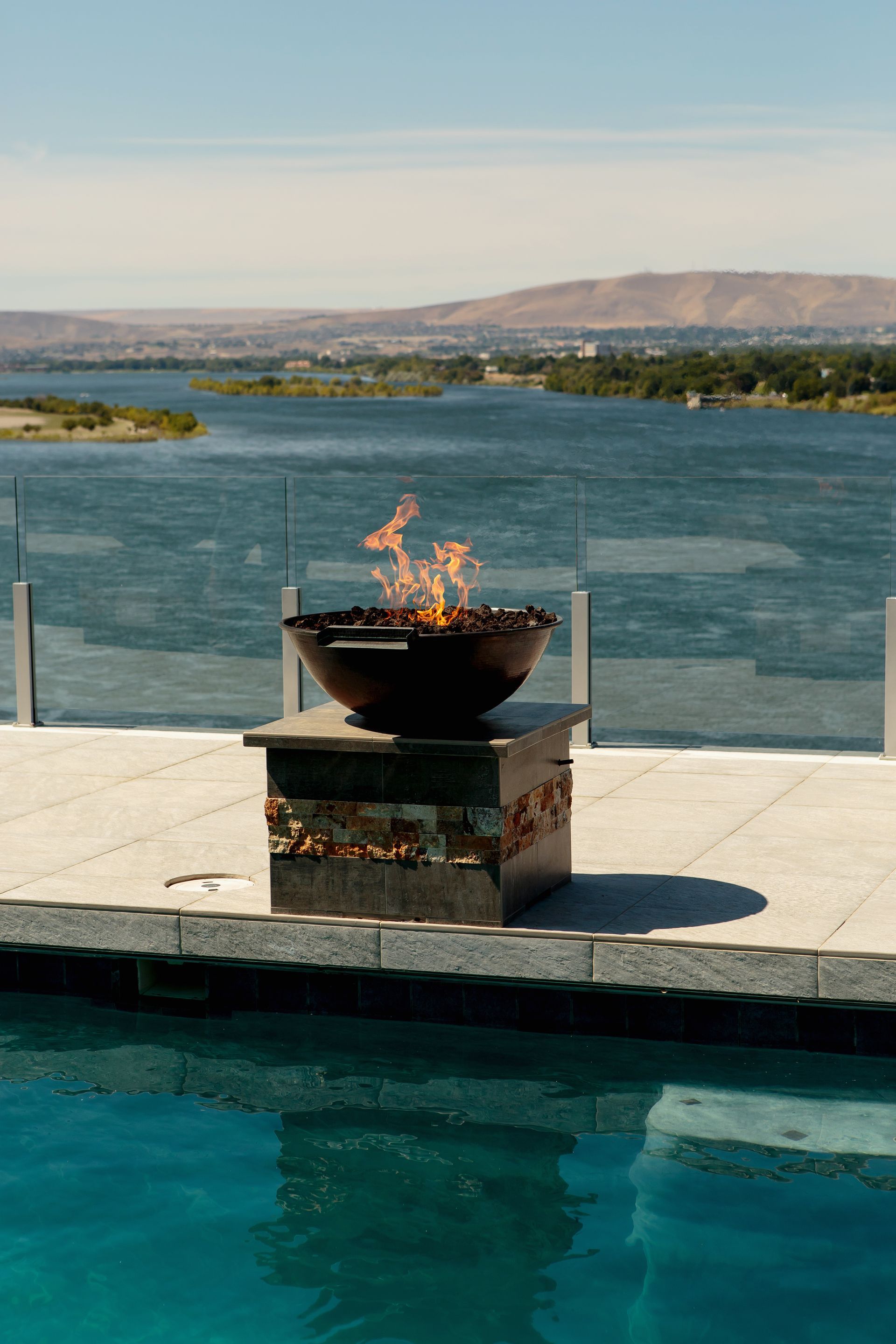 A fire pit is sitting next to a swimming pool overlooking a body of water.