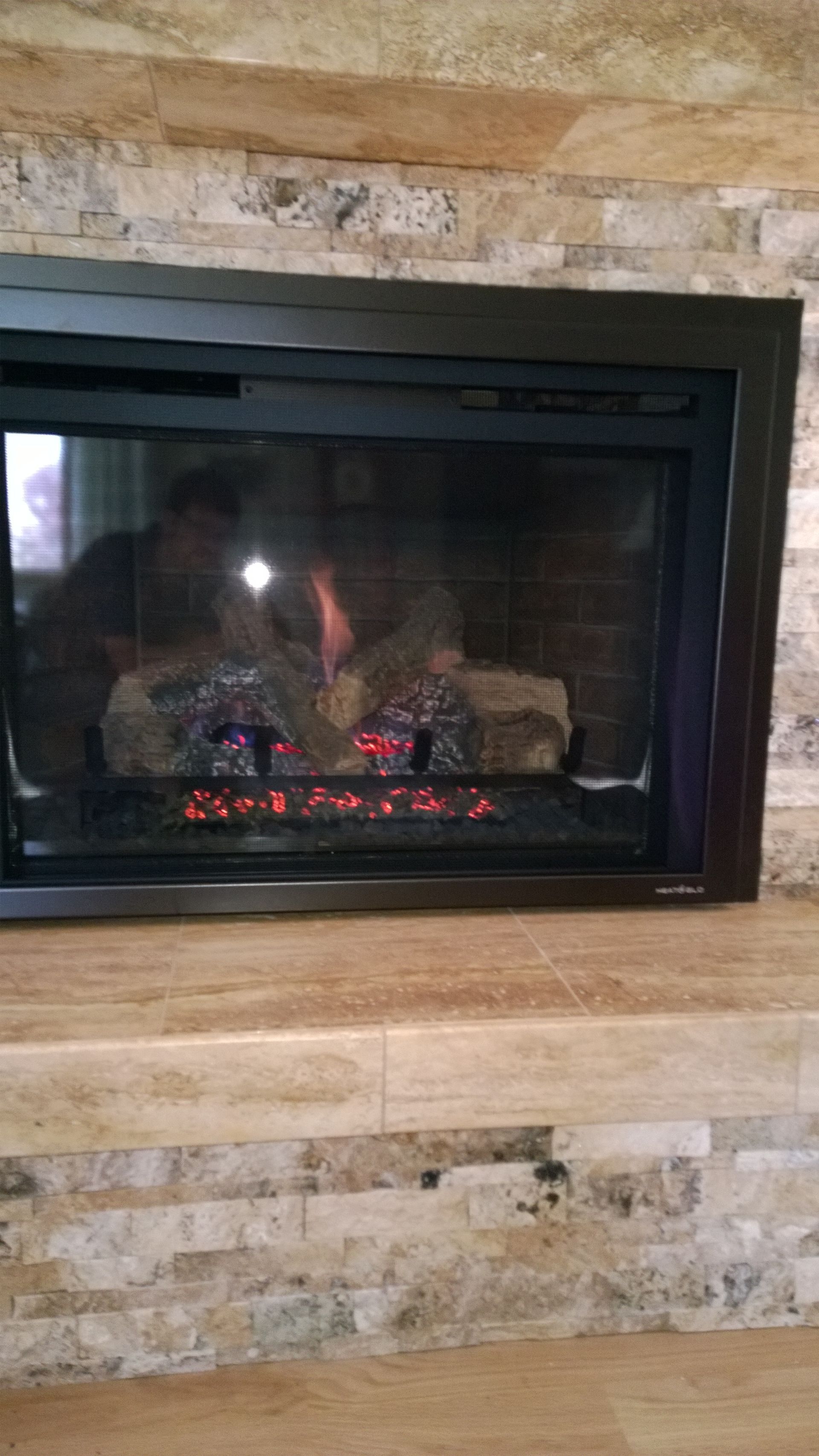 A fireplace with a glass door and a wooden mantle in a living room.