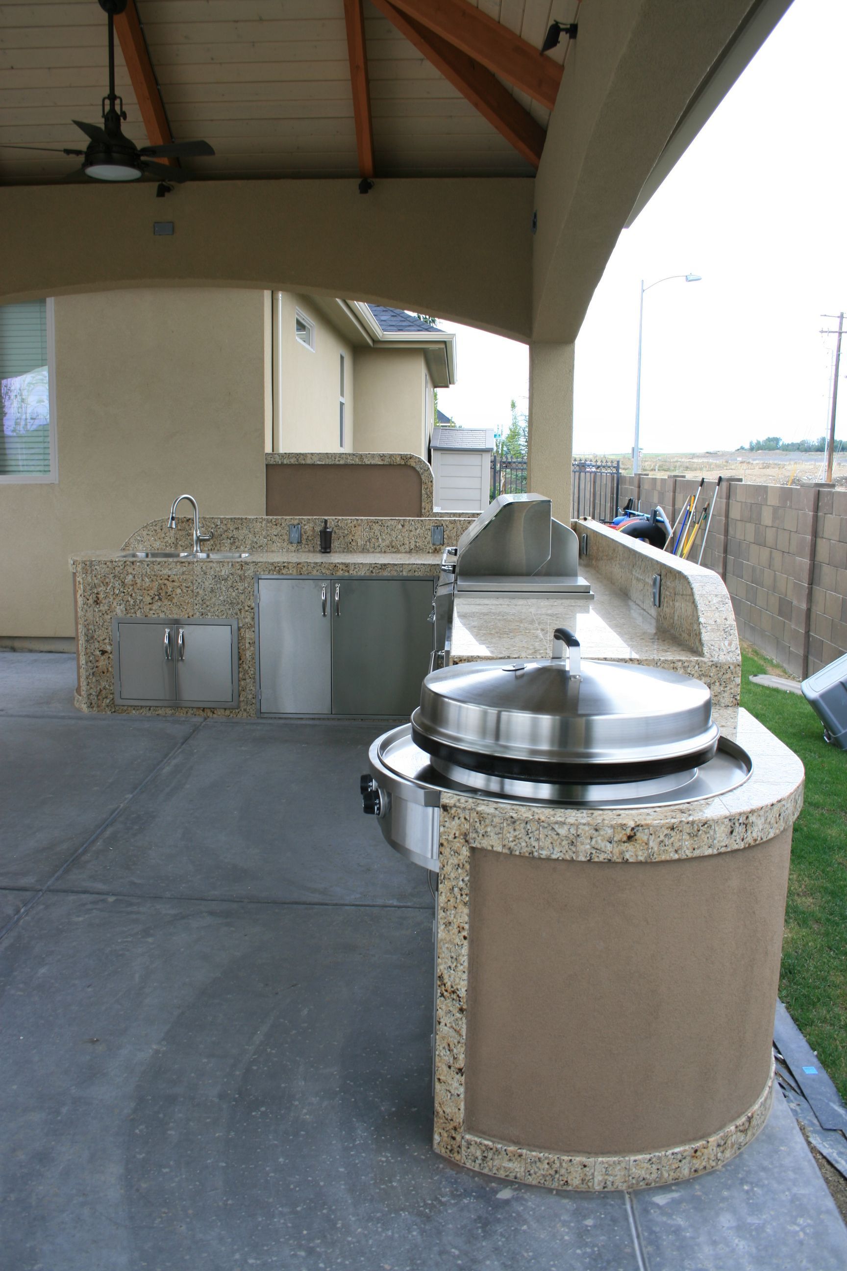 An outdoor kitchen with a stainless steel grill and a ceiling fan.