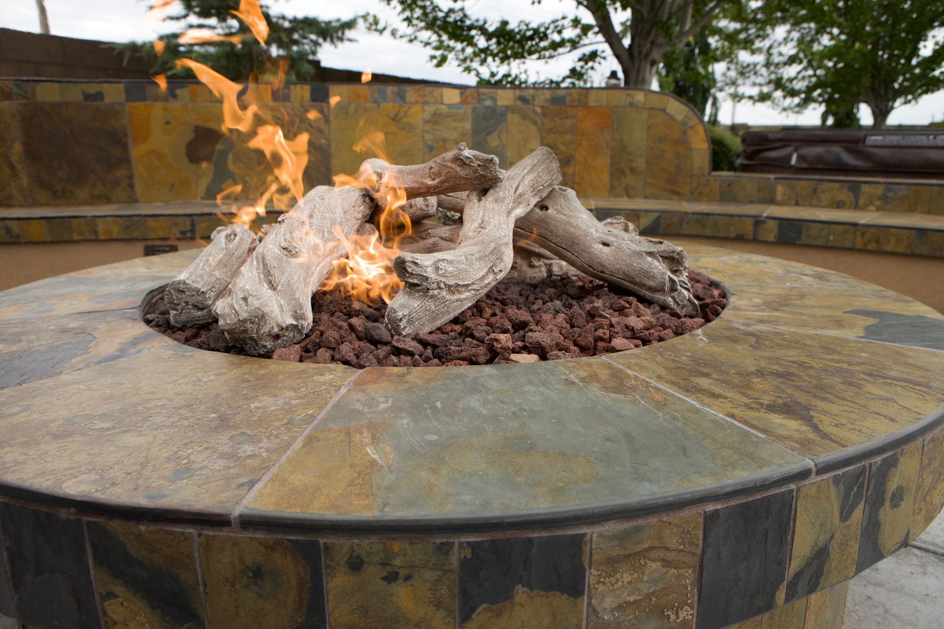 A fire pit filled with logs and rocks is sitting on a patio.