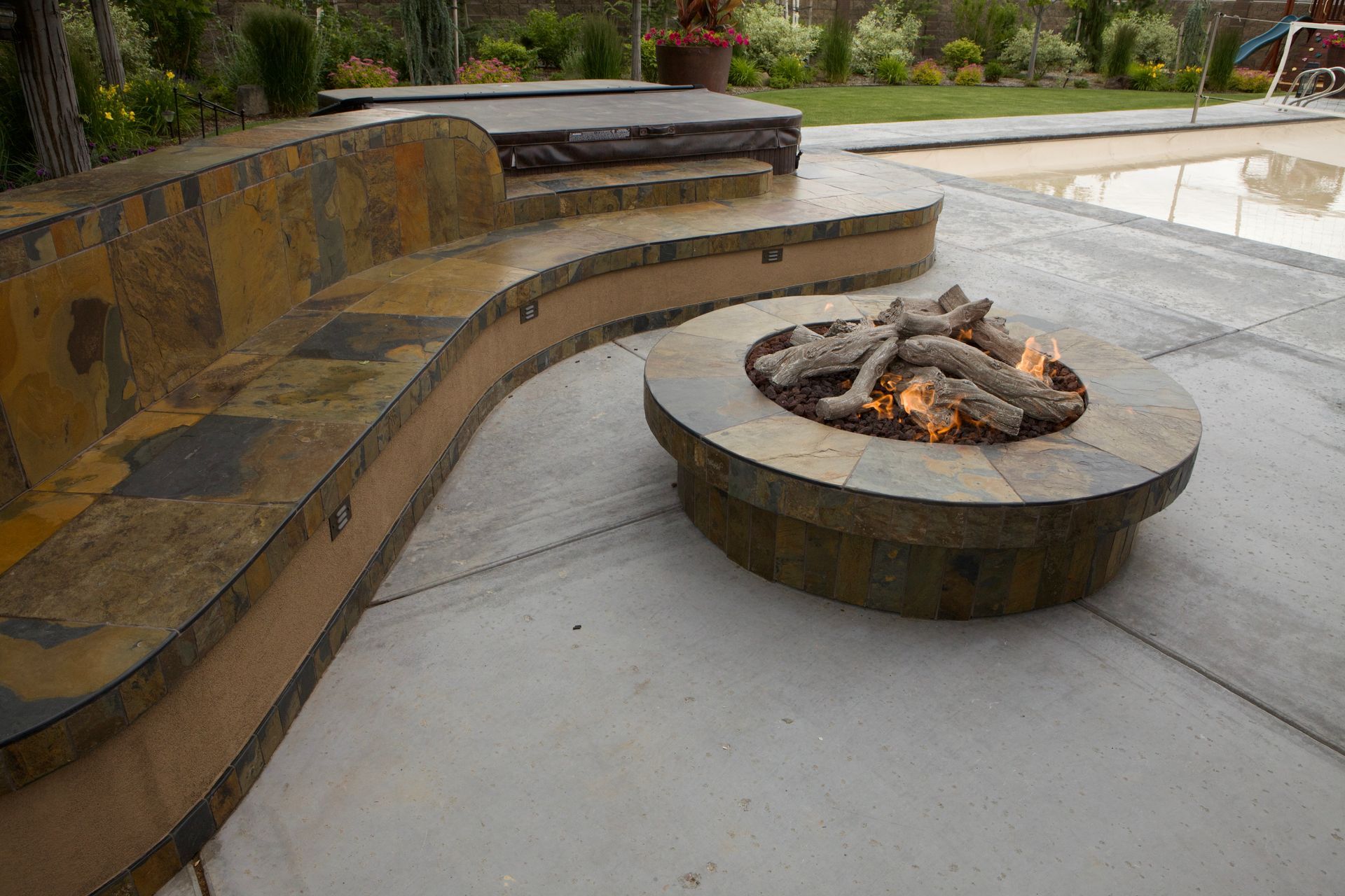 A fire pit is sitting on a patio next to a pool.