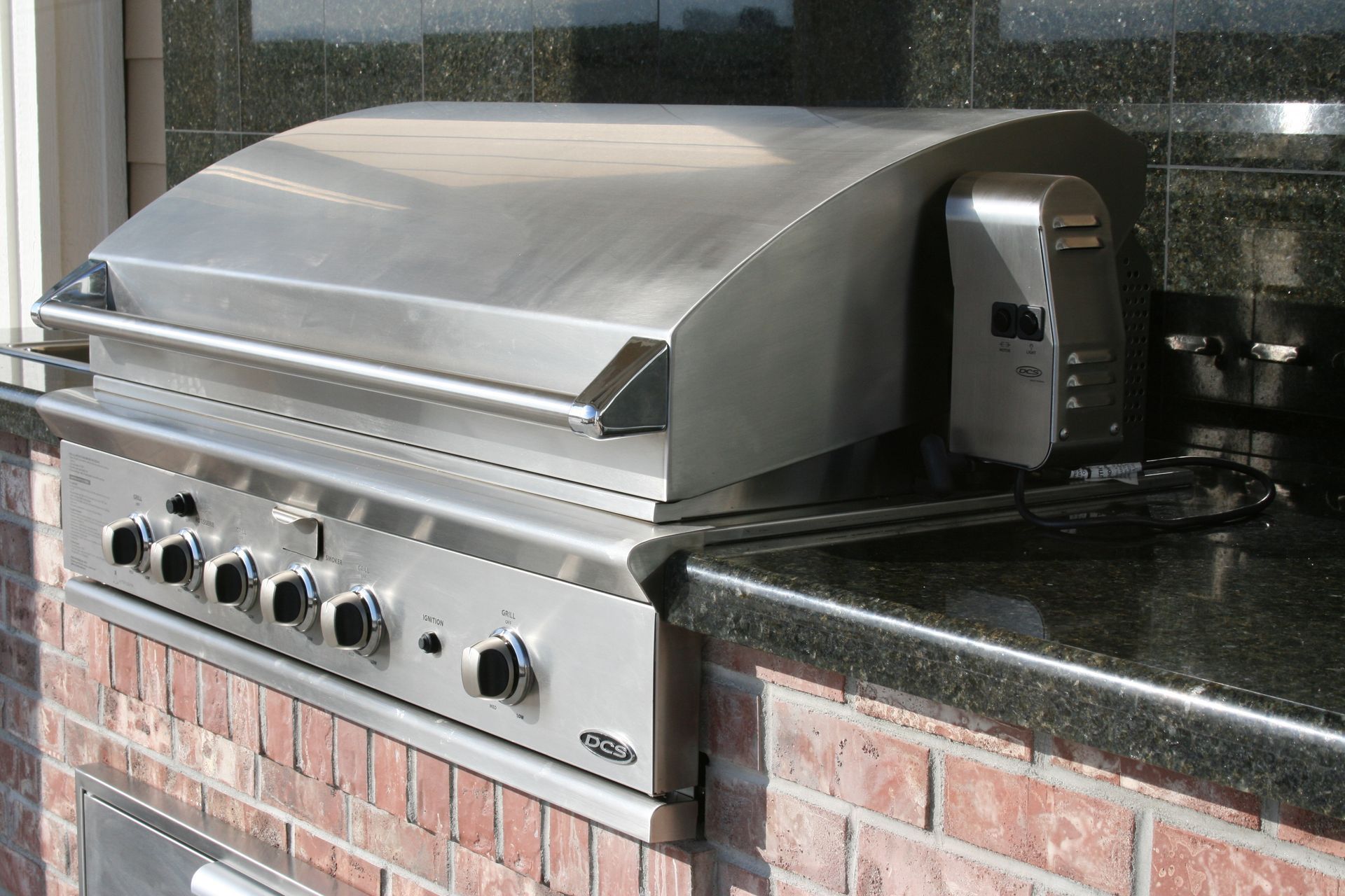 A stainless steel grill is mounted to a brick wall