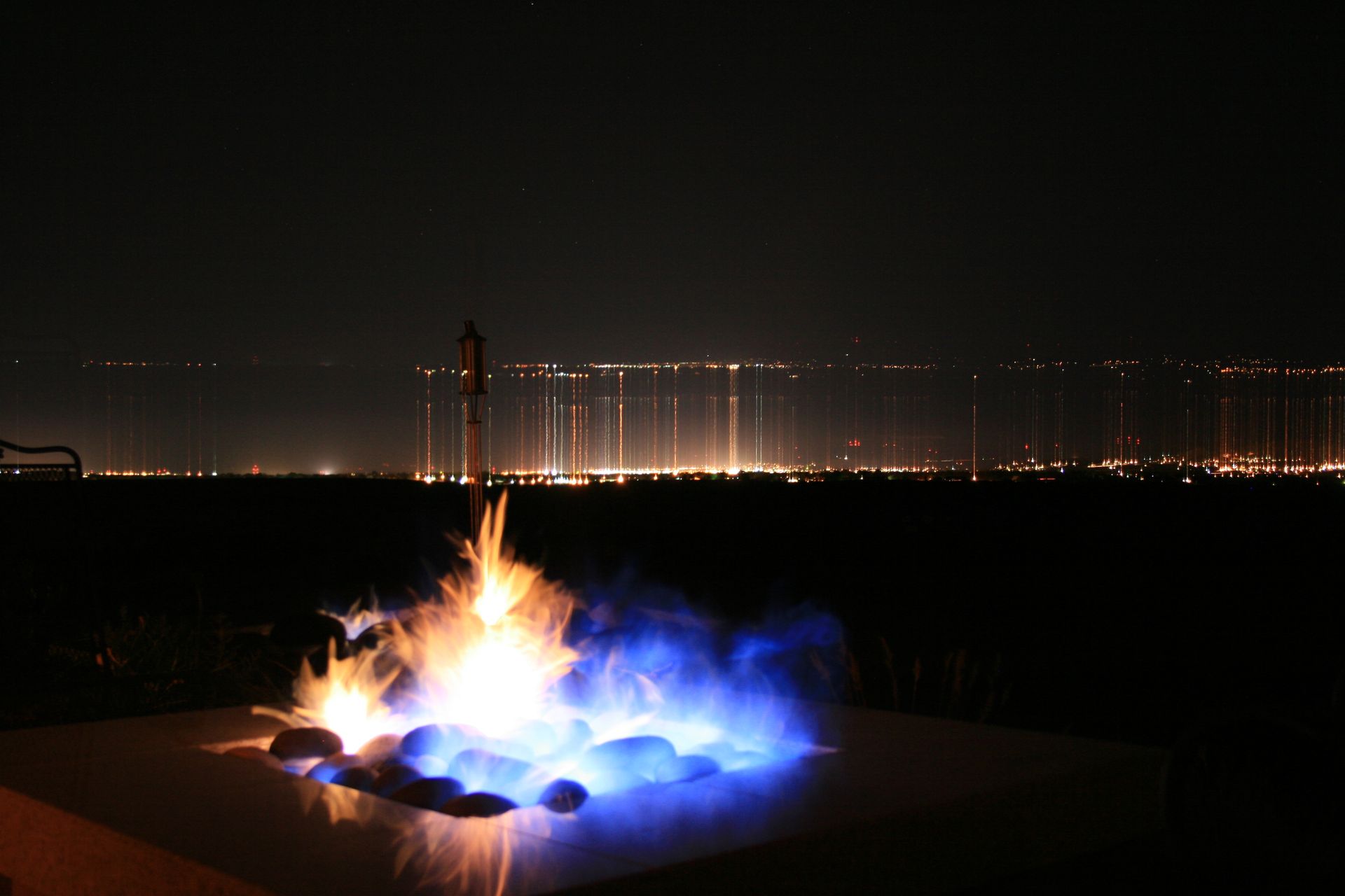 A fire pit is lit up at night with a city in the background