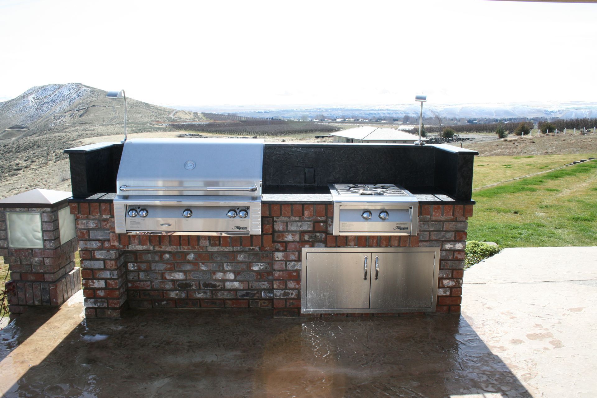 A brick and stainless steel outdoor kitchen with a grill and stove
