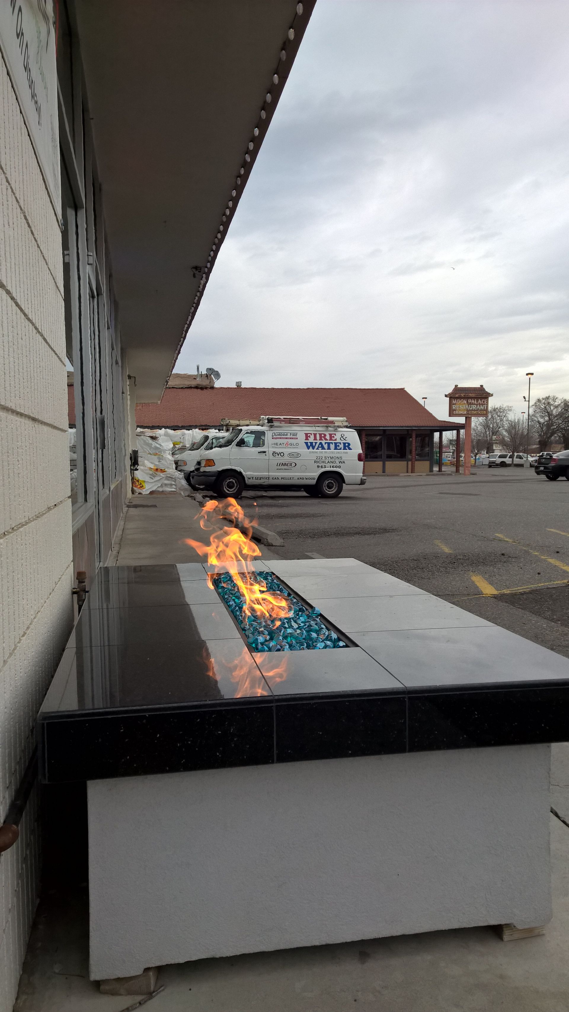 A fire pit is sitting outside of a building next to a parking lot.
