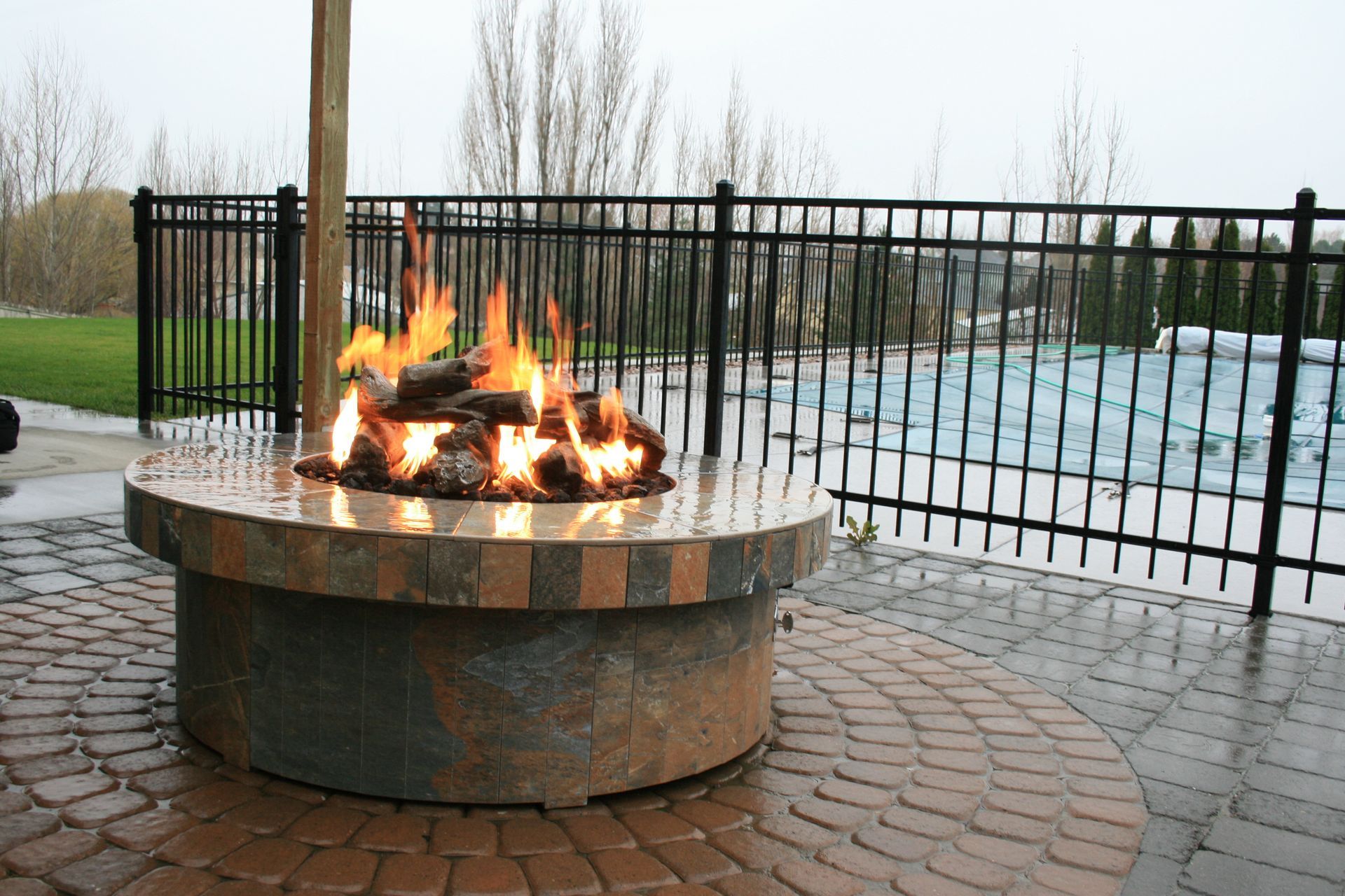 A fire pit is sitting on a brick patio next to a pool.