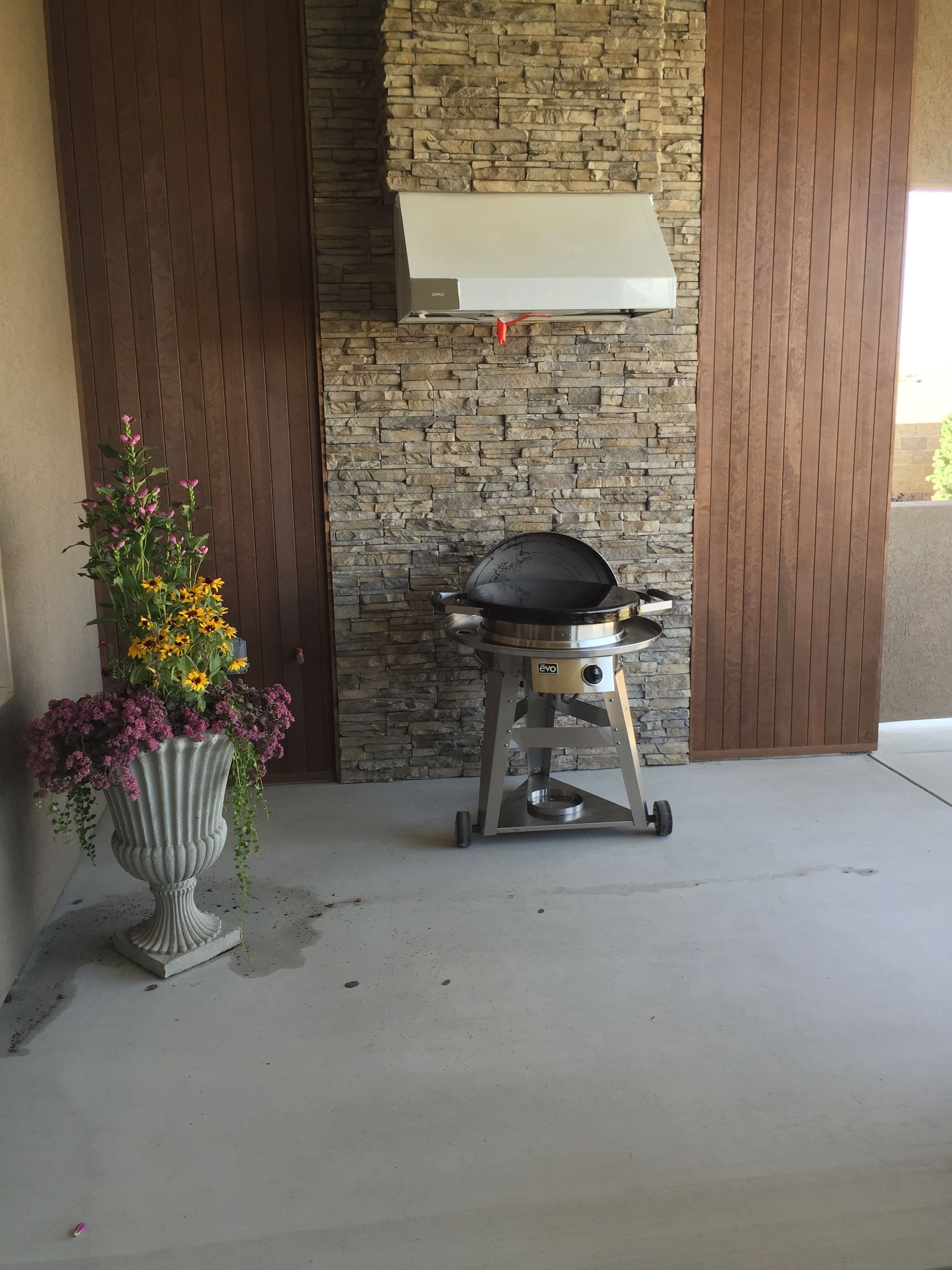 A grill is sitting in front of a stone wall next to a vase of flowers.