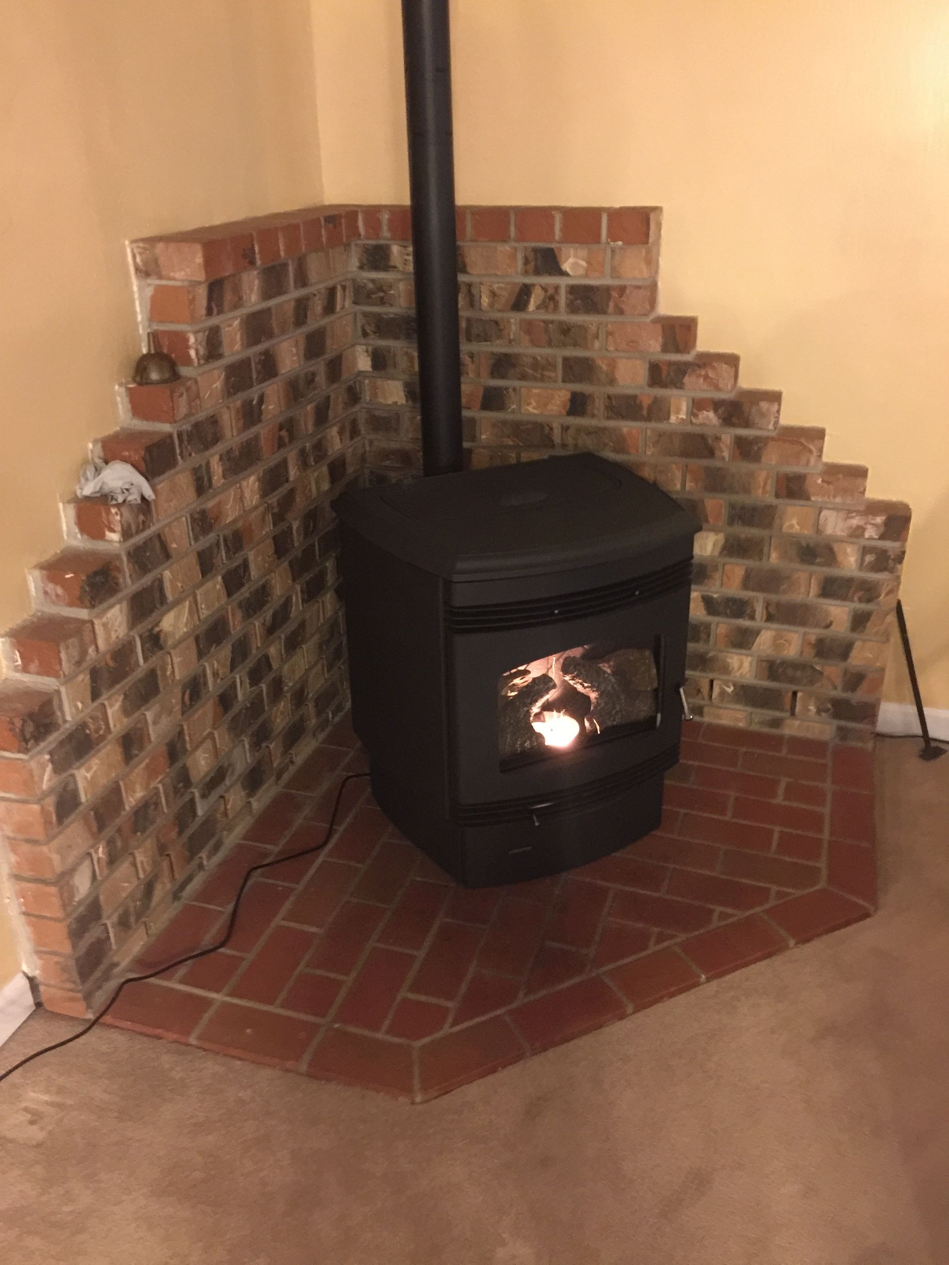 A wood stove is sitting in the corner of a room next to a brick wall.
