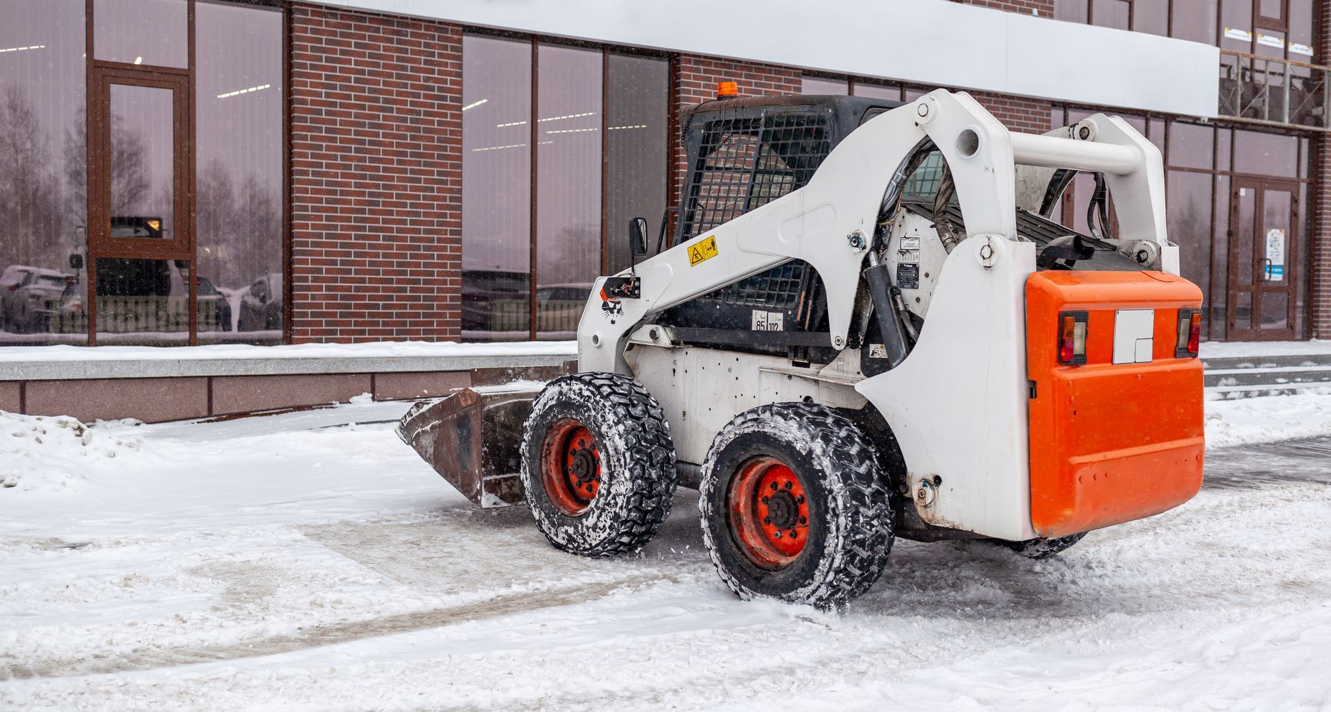 A small snowplow vehicle removing snow from a business. A small snowplow vehicle removing snow from a business.