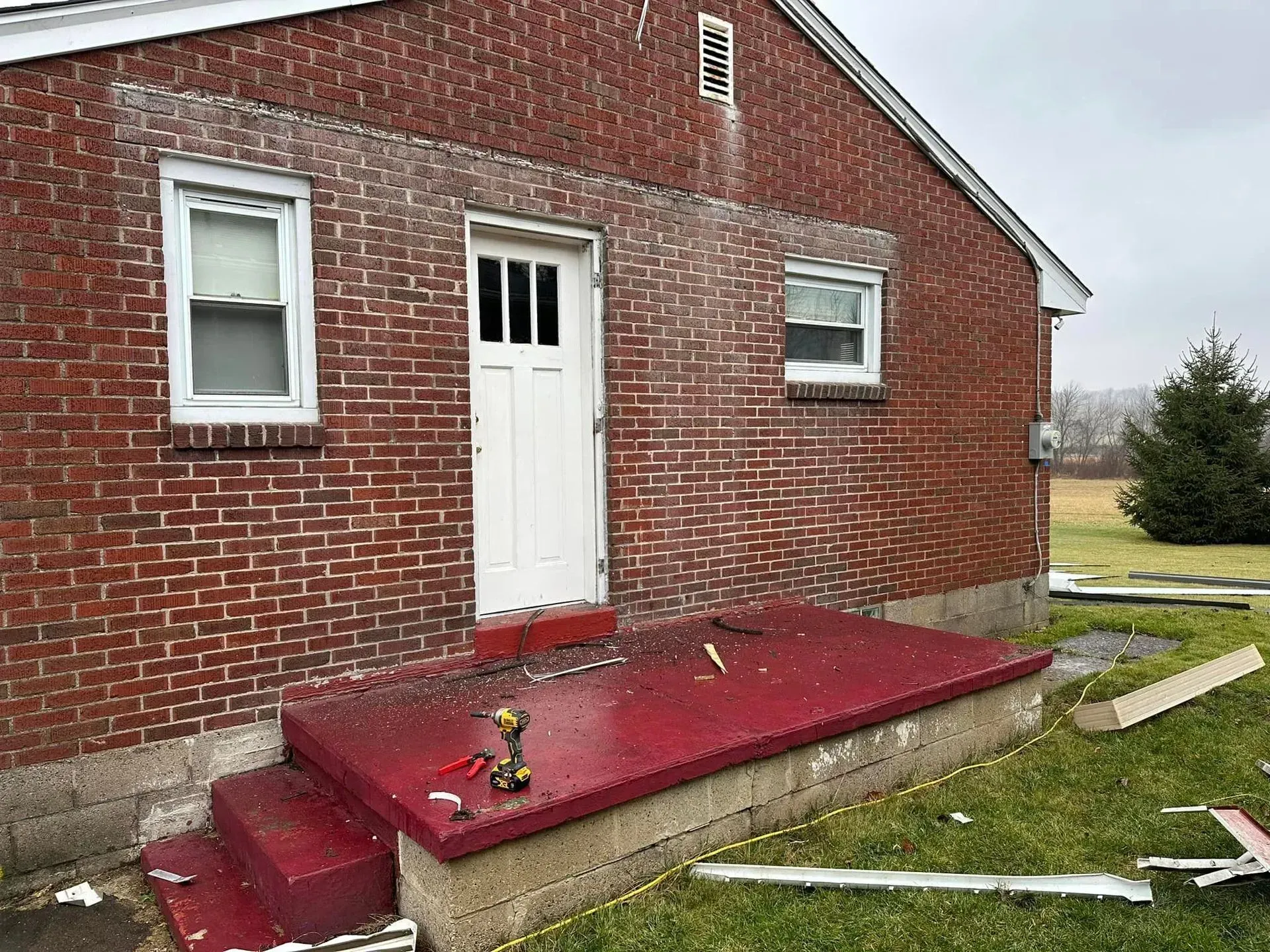A red porch is being built on the side of a brick house.
