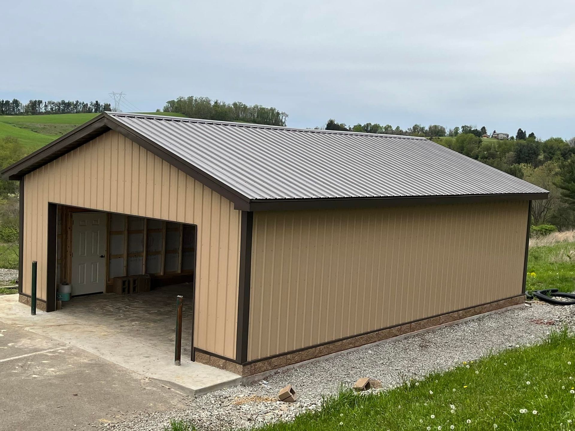 A large metal garage with a gray roof is sitting in the middle of a grassy field.