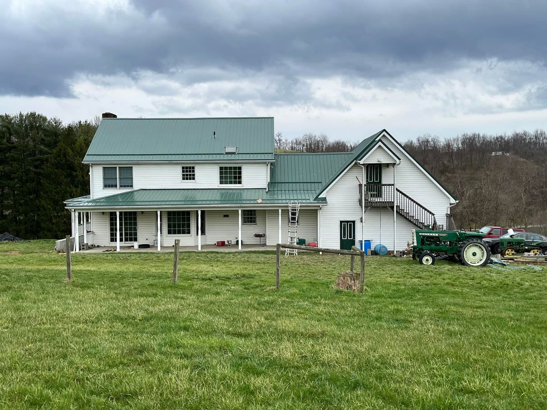 A white house with a green roof is sitting in the middle of a grassy field.