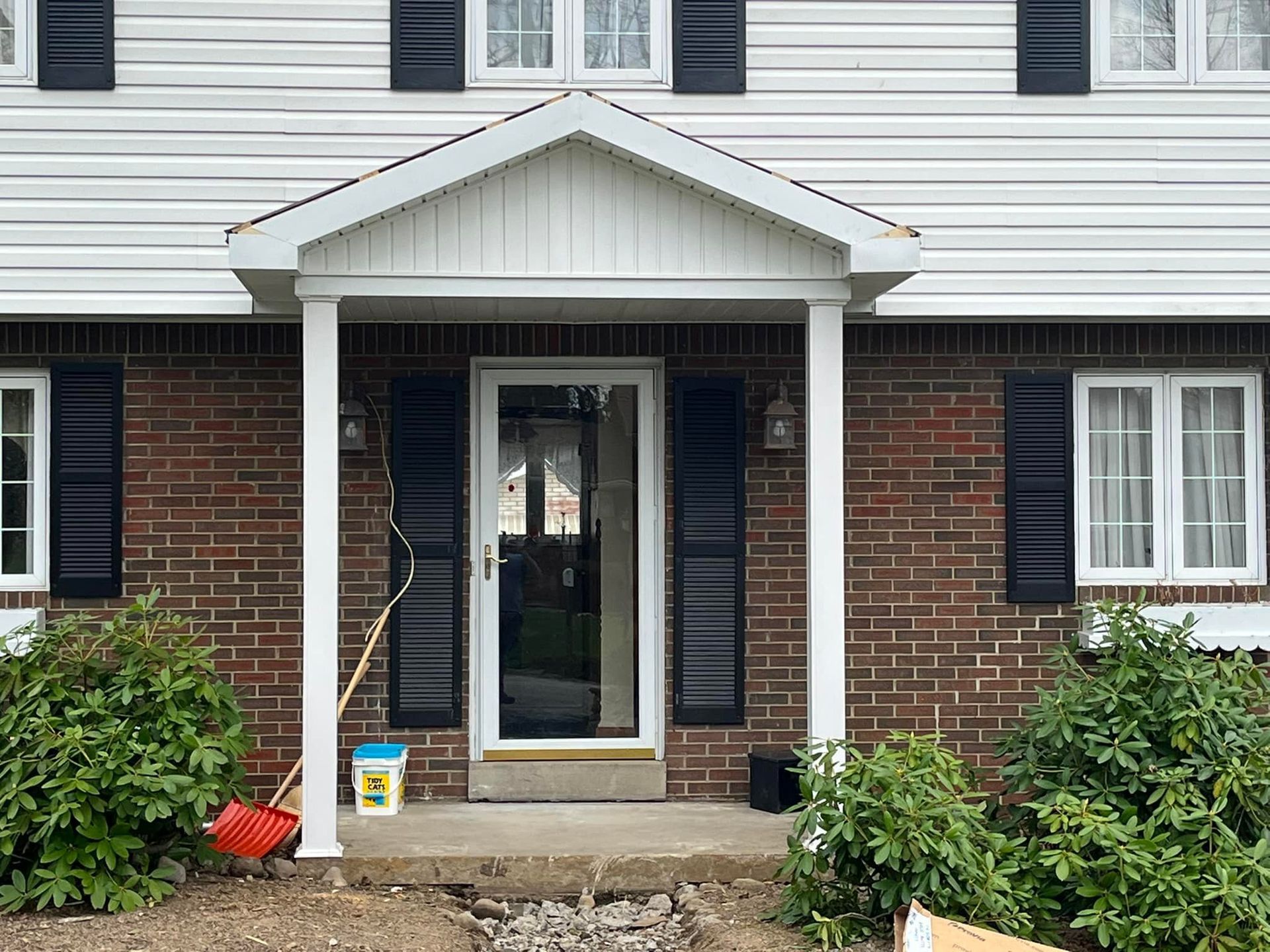 The front of a brick house with black shutters and a white porch.