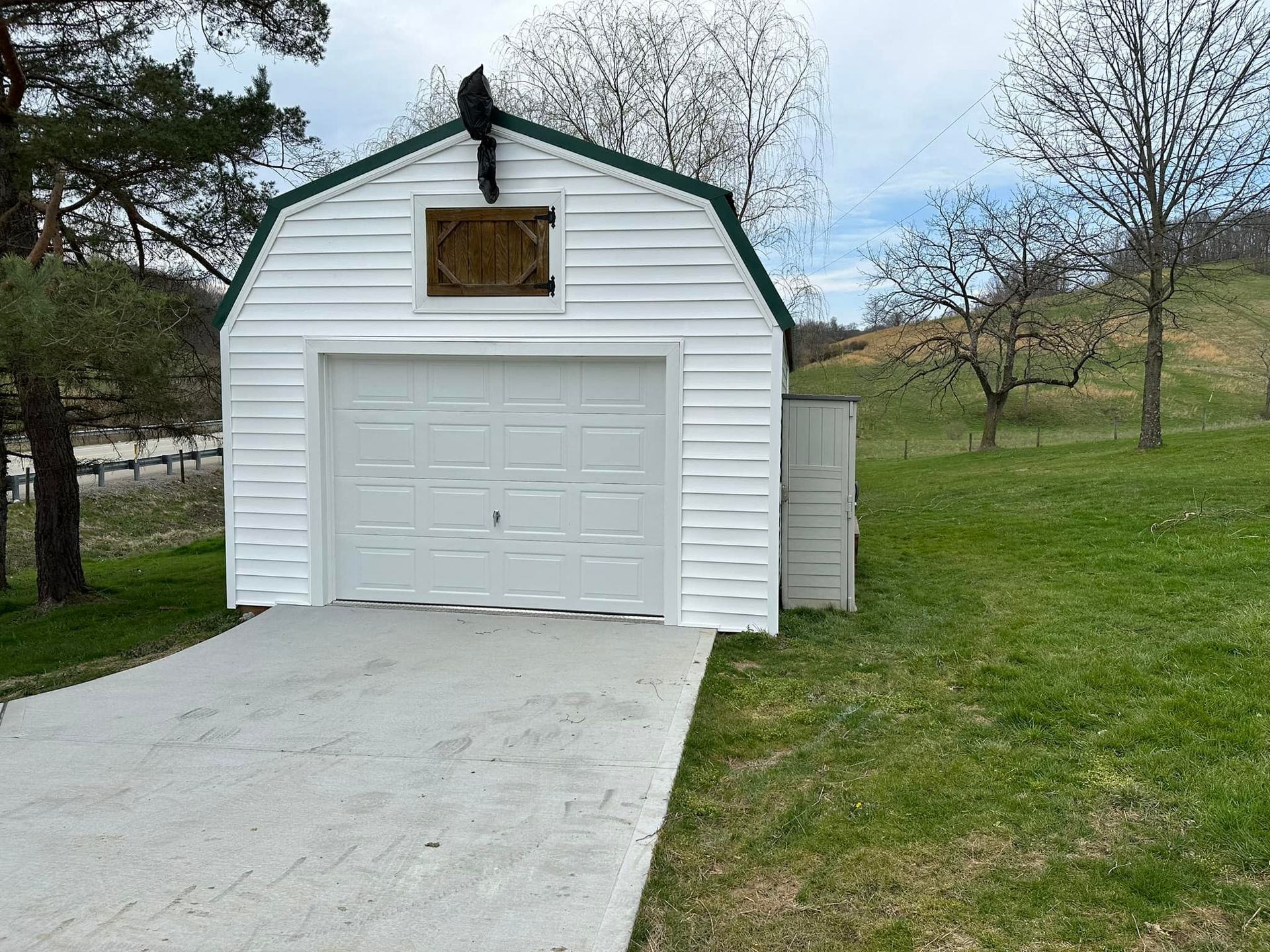 A white garage with a green trim is sitting in the middle of a grassy field.