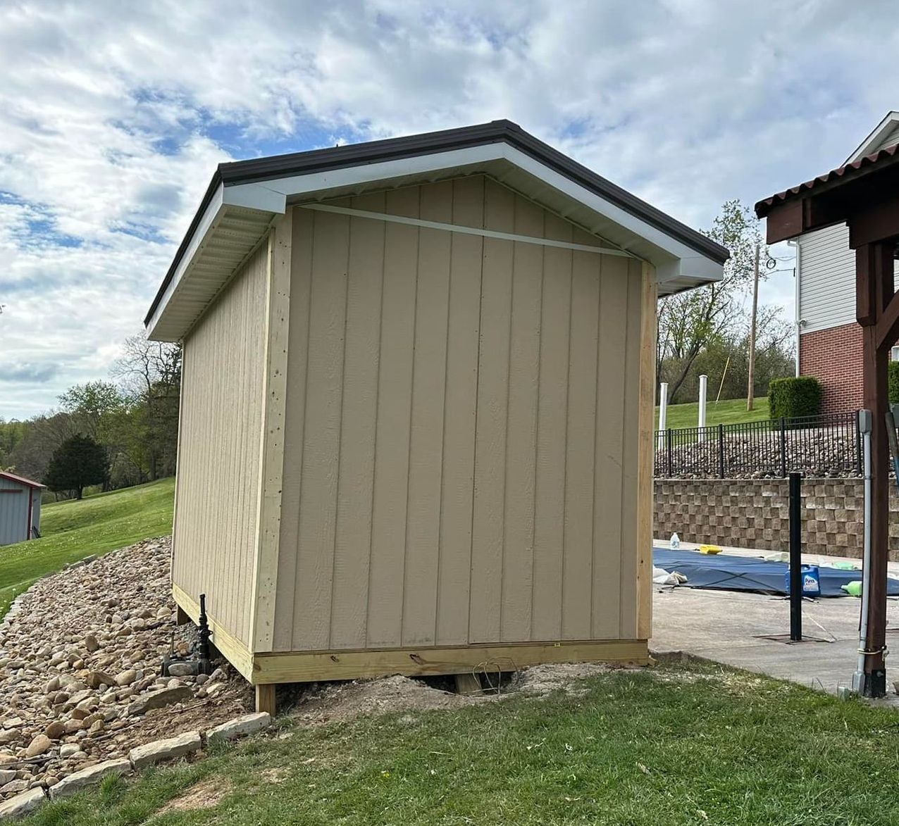 A small shed is sitting on top of a grassy hill next to a house.