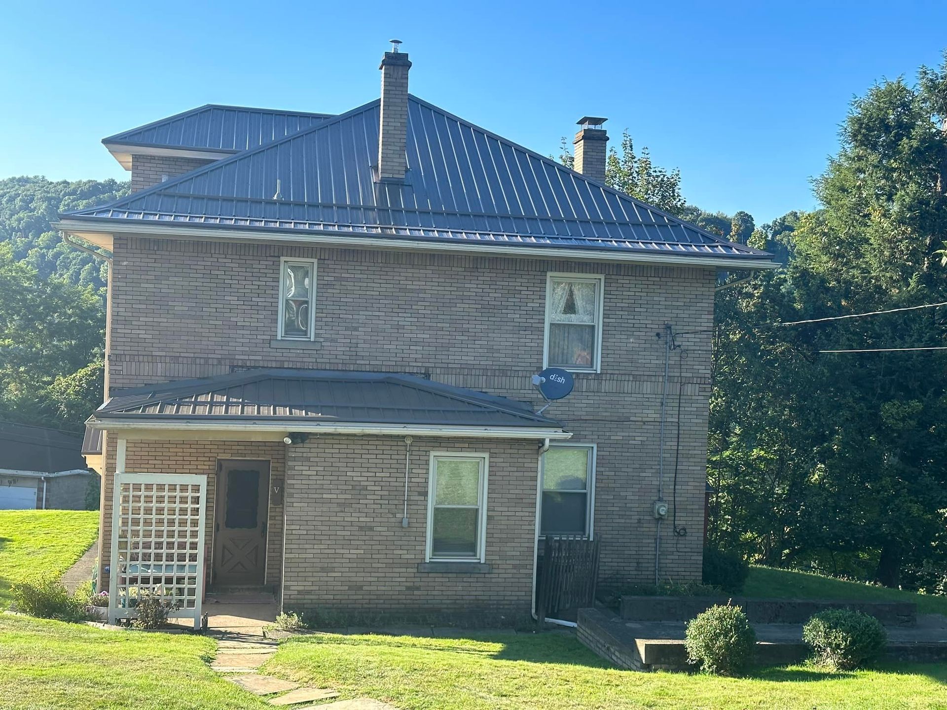 A brick house with a metal roof is sitting in the middle of a grassy field.