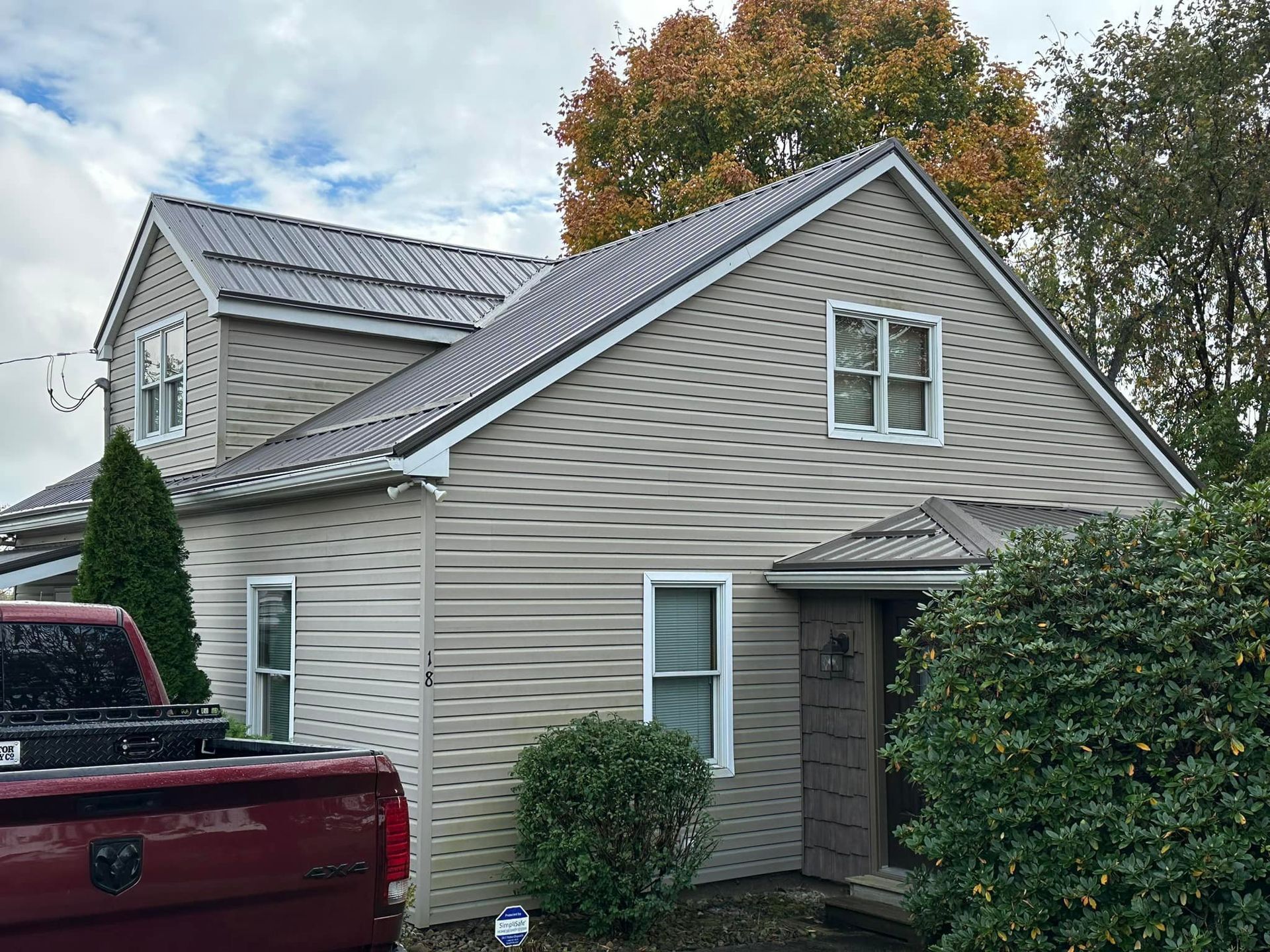 A red truck is parked in front of a house with a metal roof.