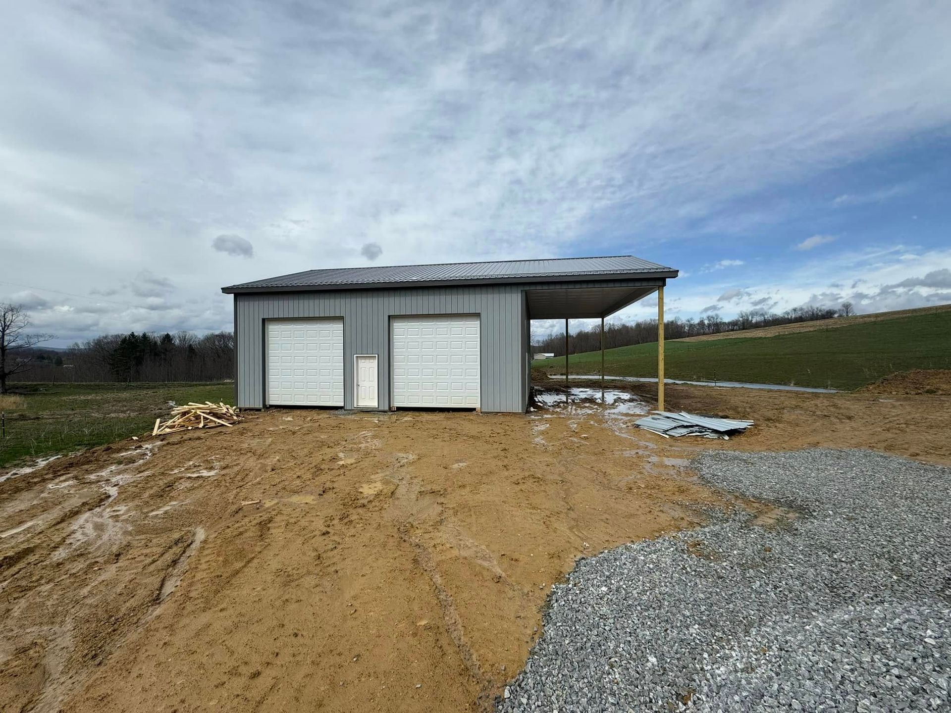 A garage with two garage doors and a carport is sitting in the middle of a dirt field.