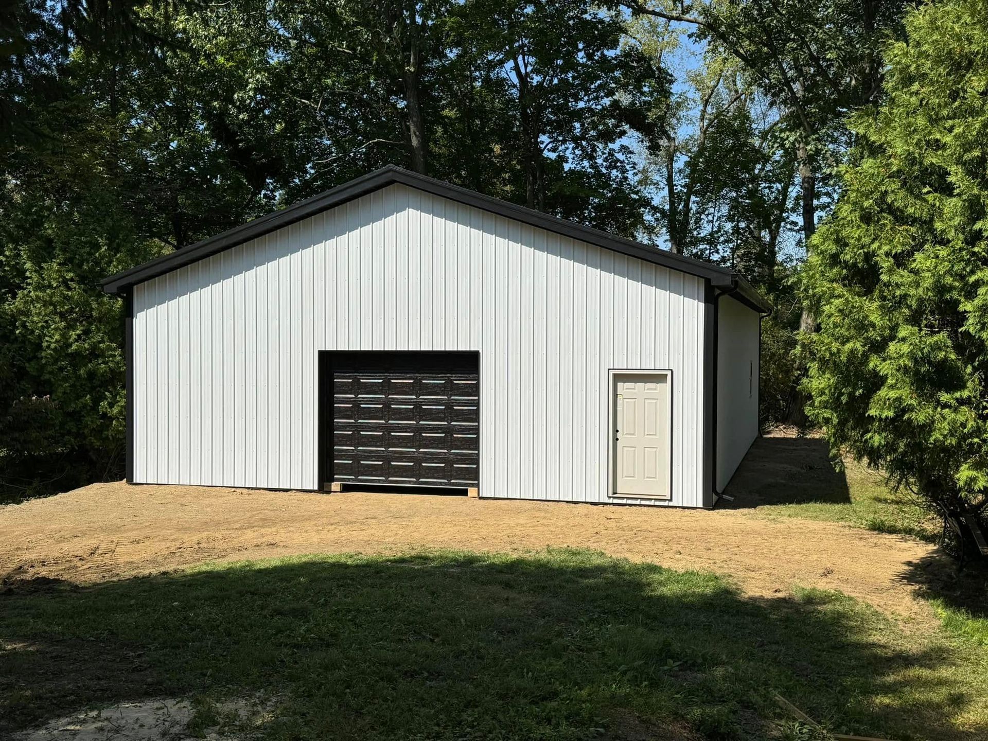 A white garage with a black garage door is sitting in the middle of a grassy field.