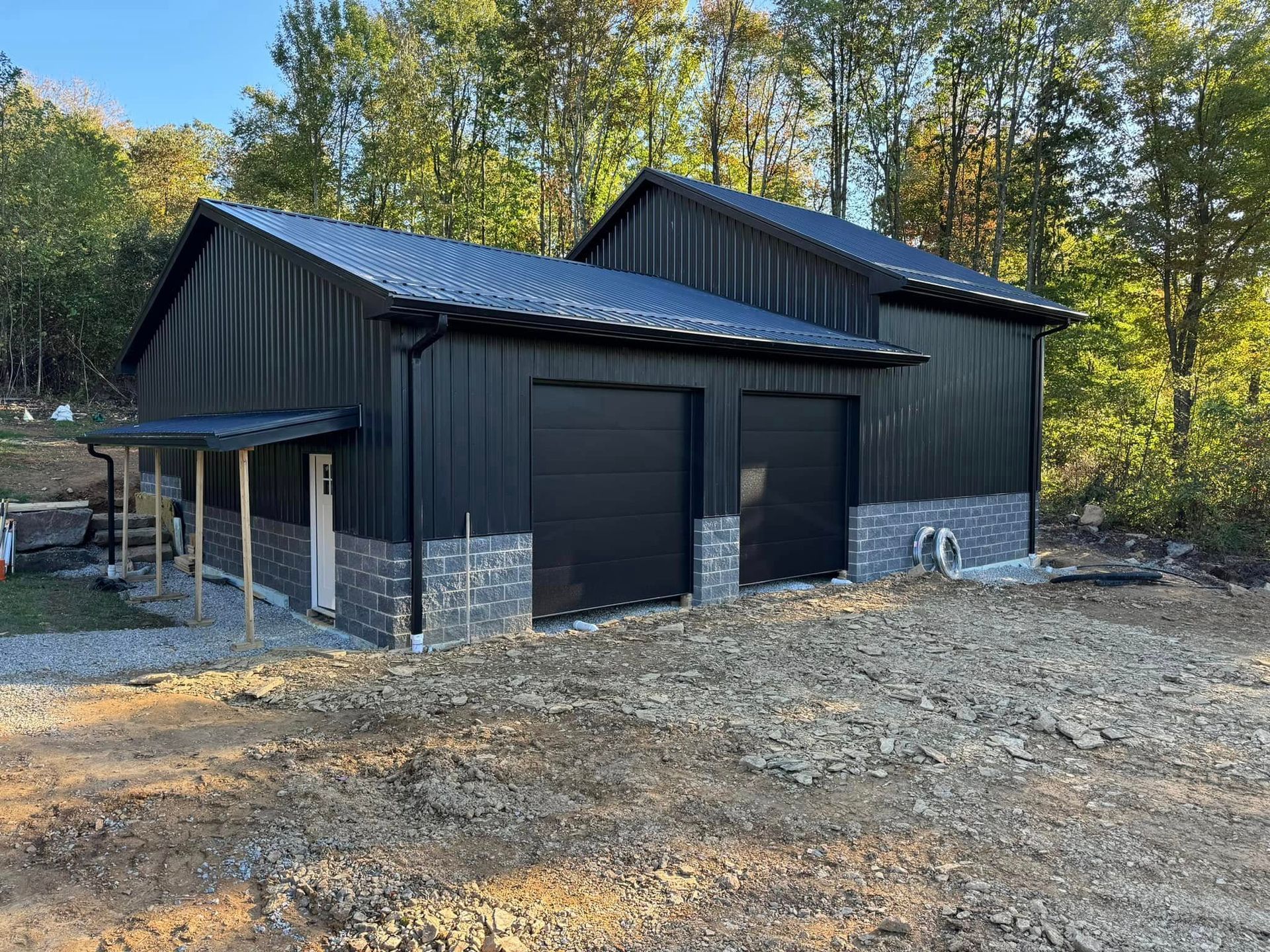 A black garage with two garage doors is sitting in the middle of a dirt field.