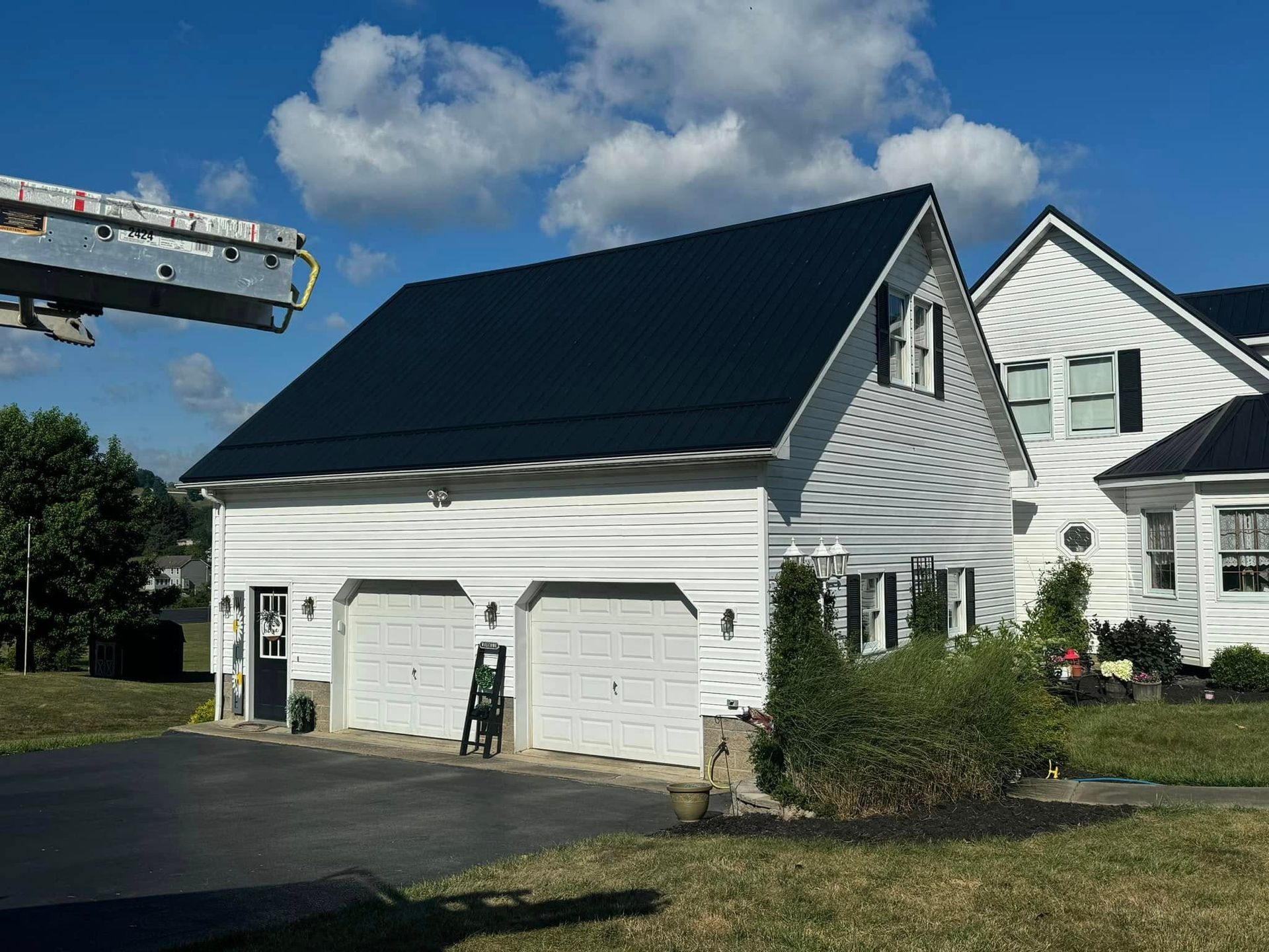 A white house with a black roof and a ladder in front of it.