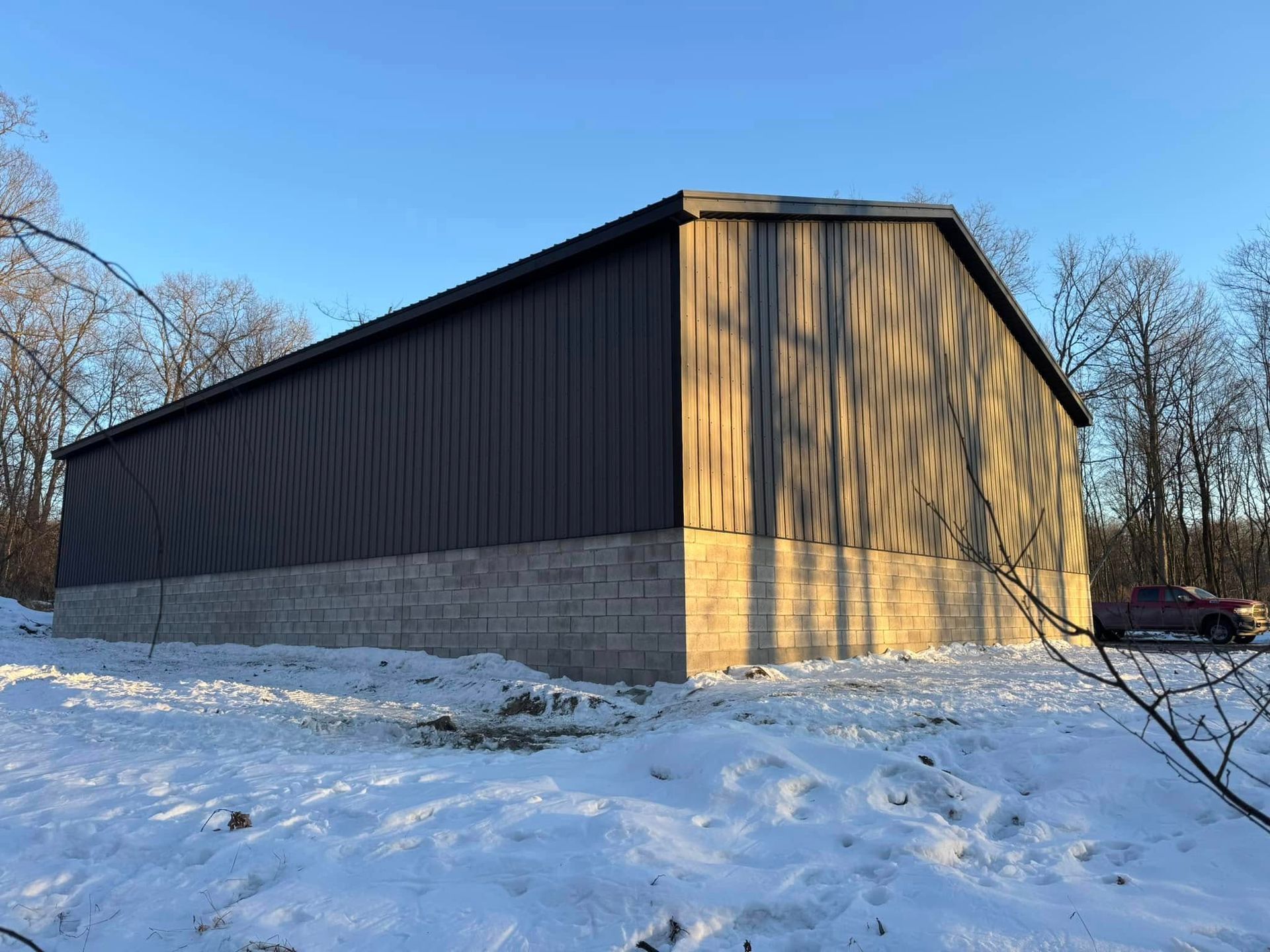 A large barn is sitting in the middle of a snow covered field.