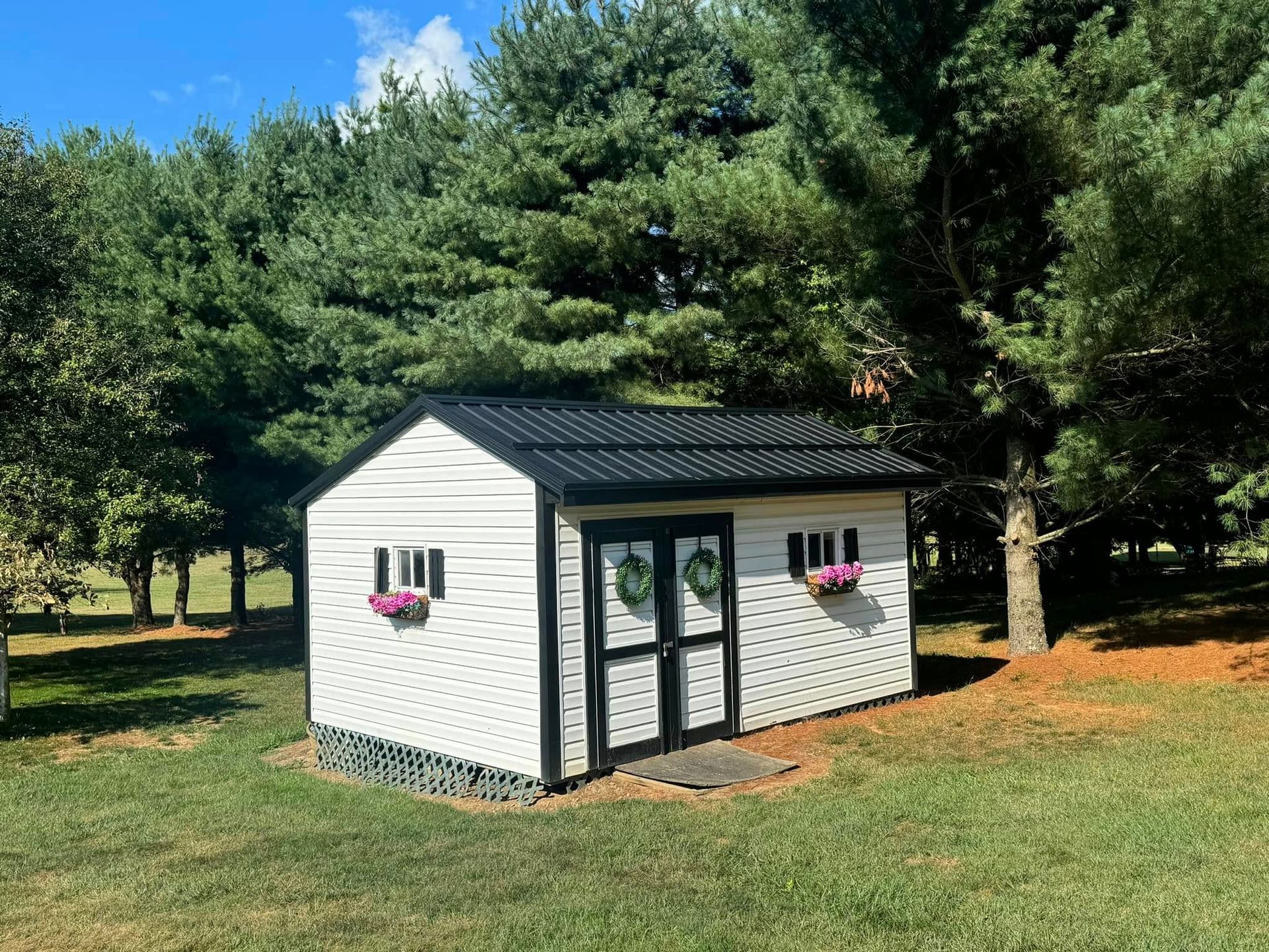 A white and black shed is sitting in the middle of a lush green field.