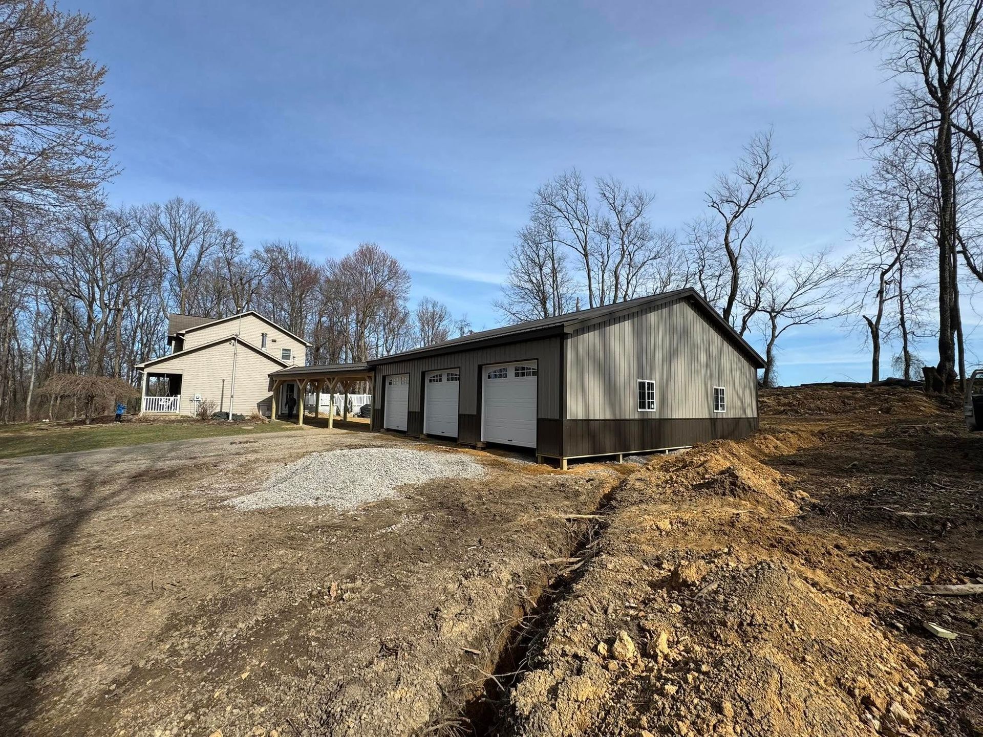 A large garage is sitting in the middle of a dirt field next to a house.