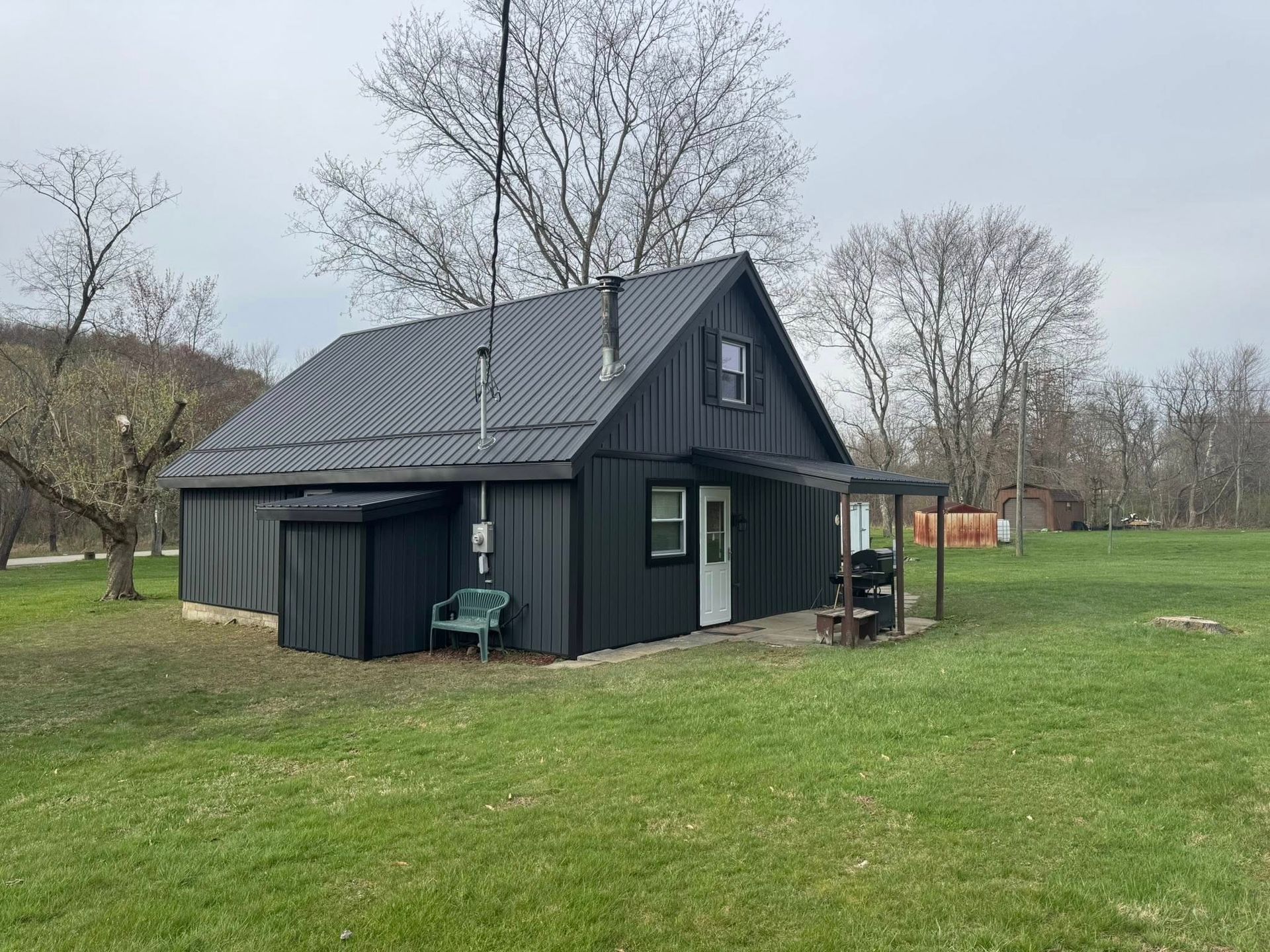 A small black house is sitting in the middle of a grassy field.