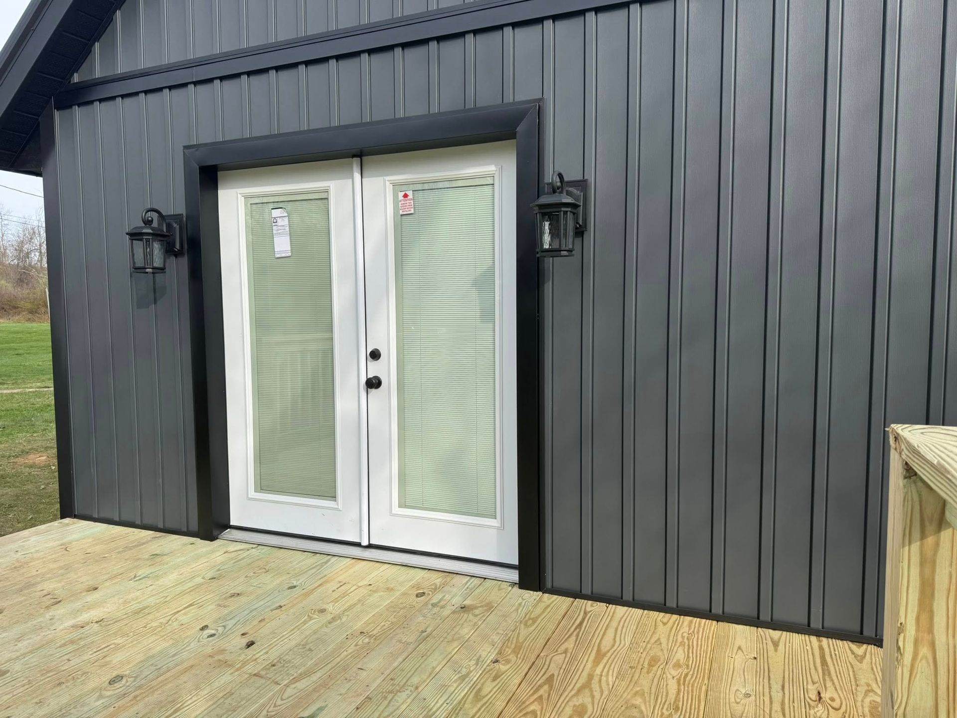 A black building with white doors and a wooden deck.