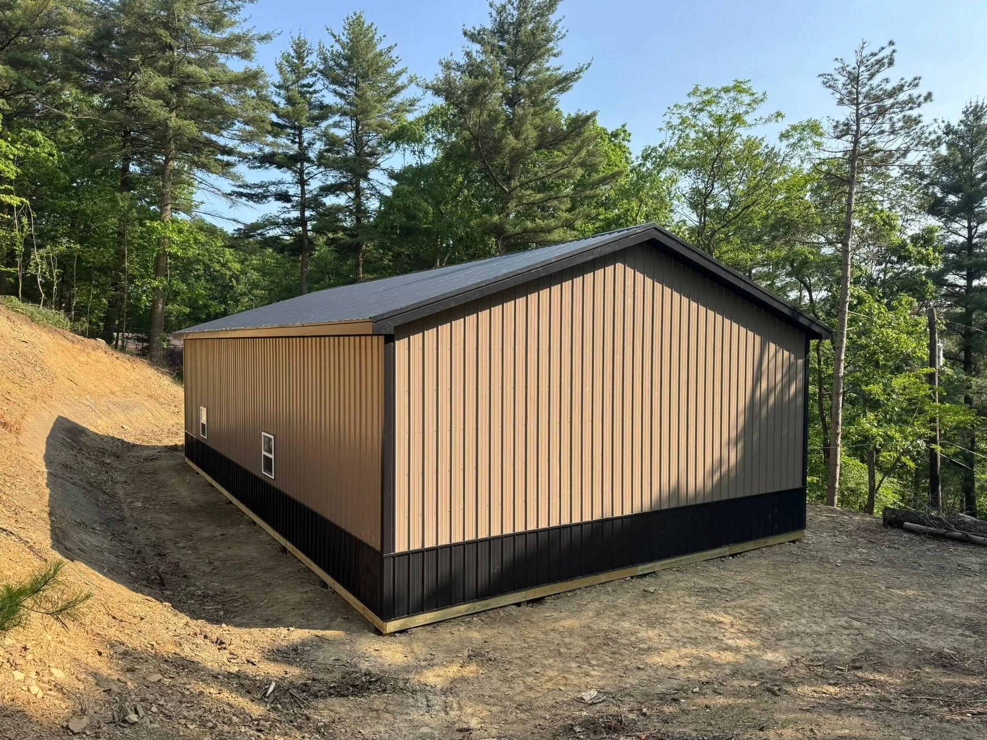 A large metal building is sitting on top of a dirt hill surrounded by trees.