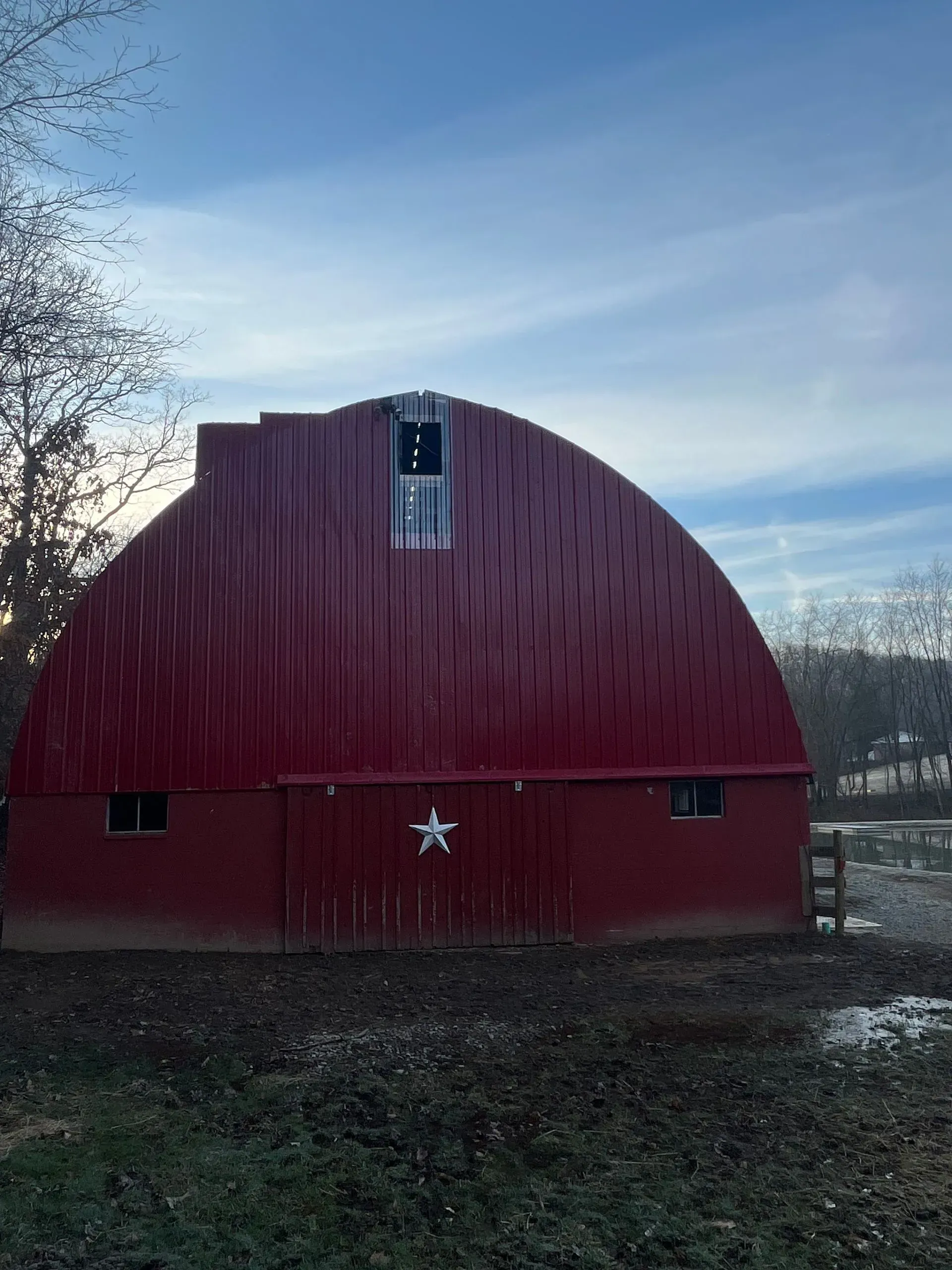 A red barn with a star on the door is sitting in the middle of a field.