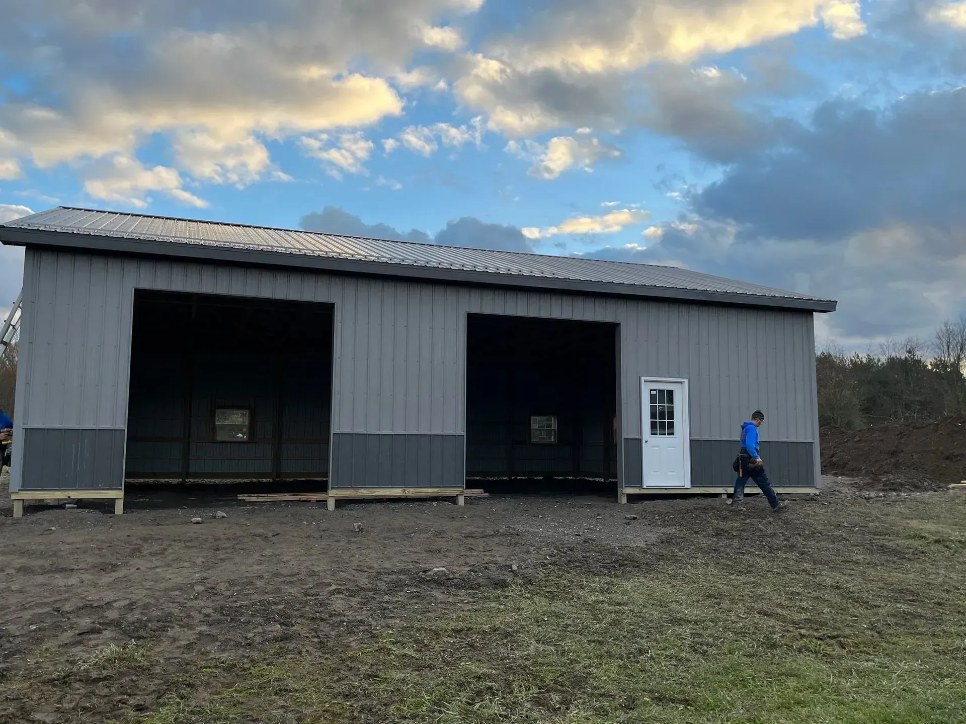 A man is walking in front of a large metal building.