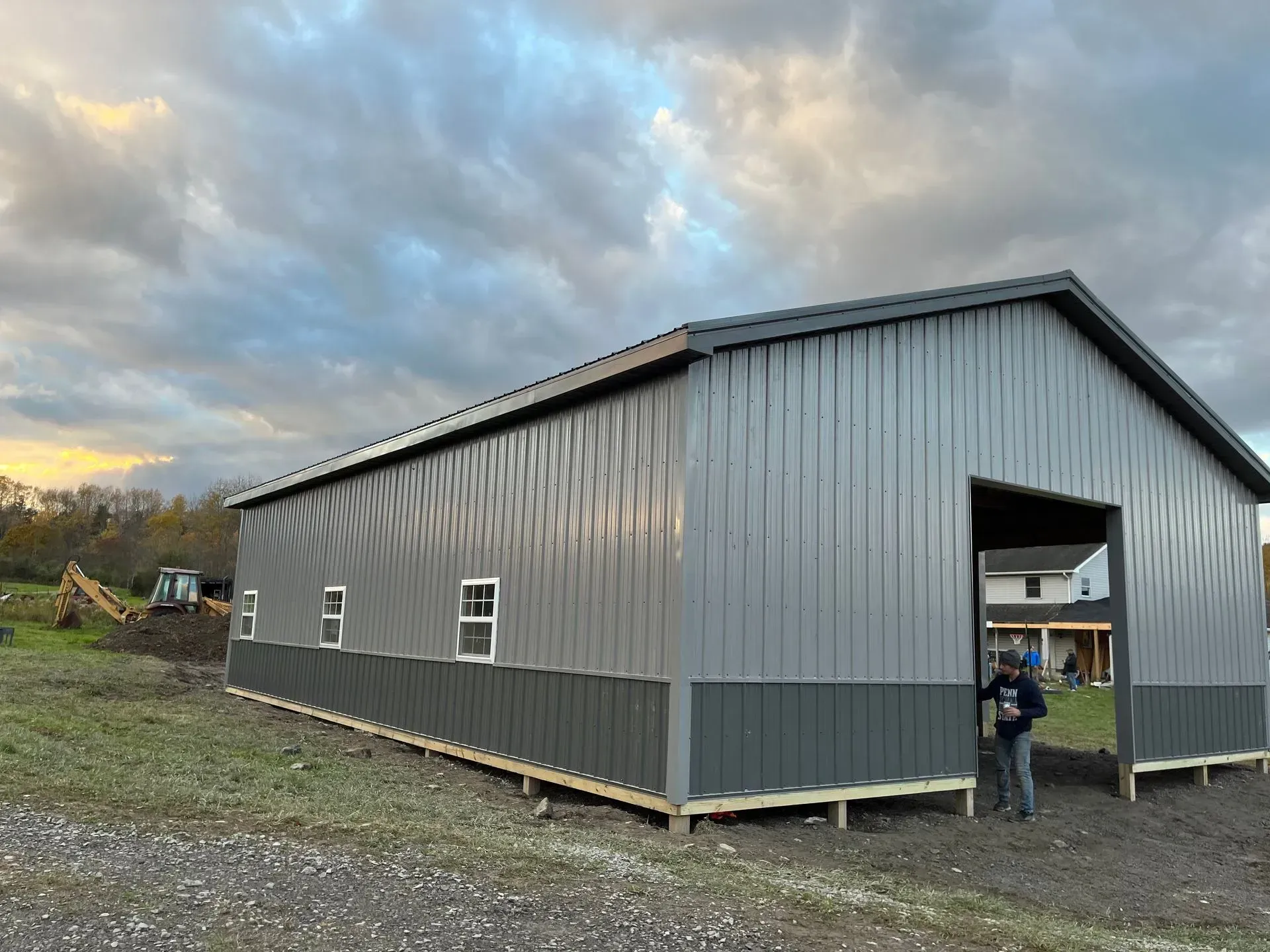 A man is standing in front of a large metal building under construction.
