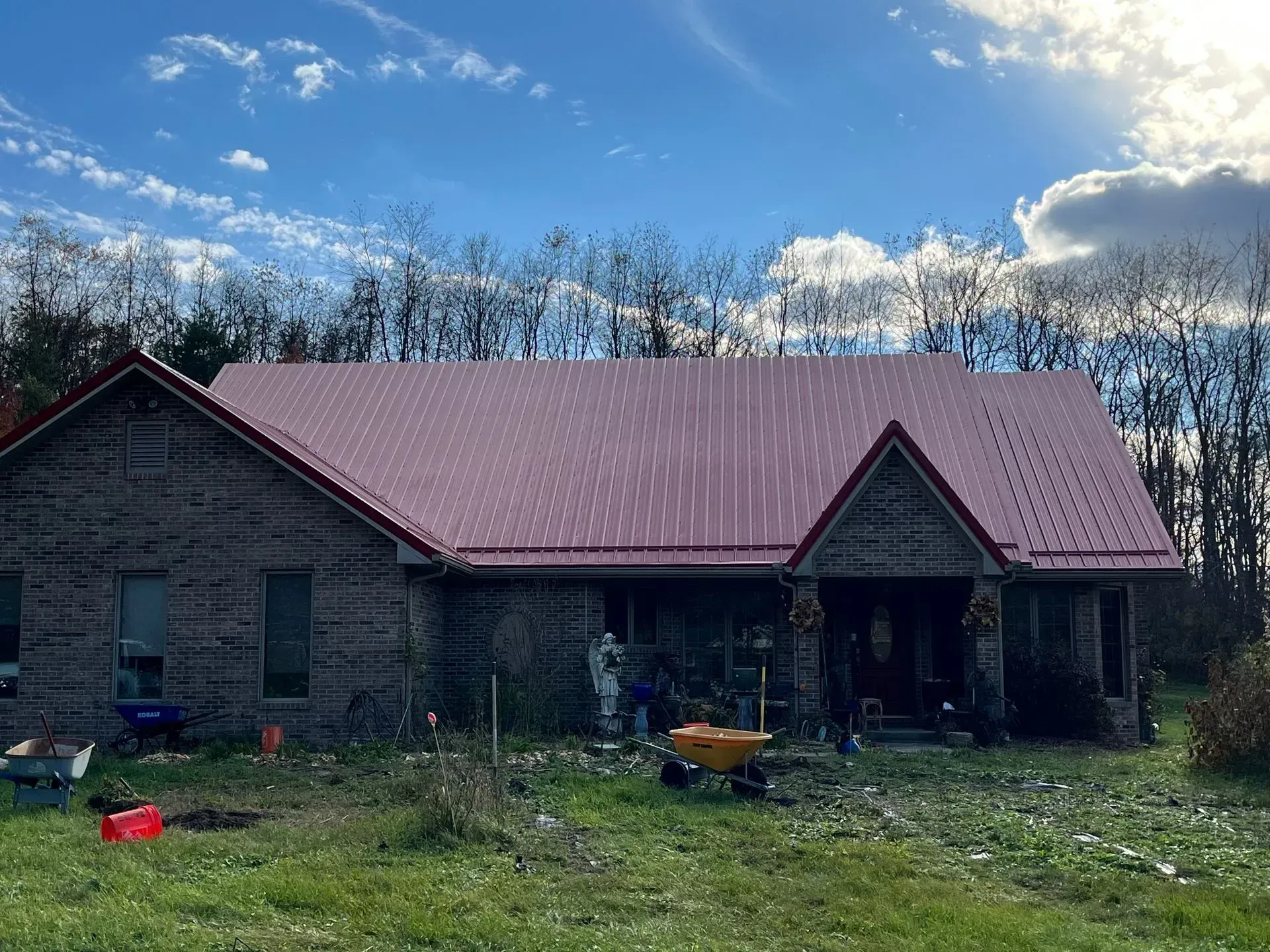 A brick house with a red roof and a wheelbarrow in front of it.