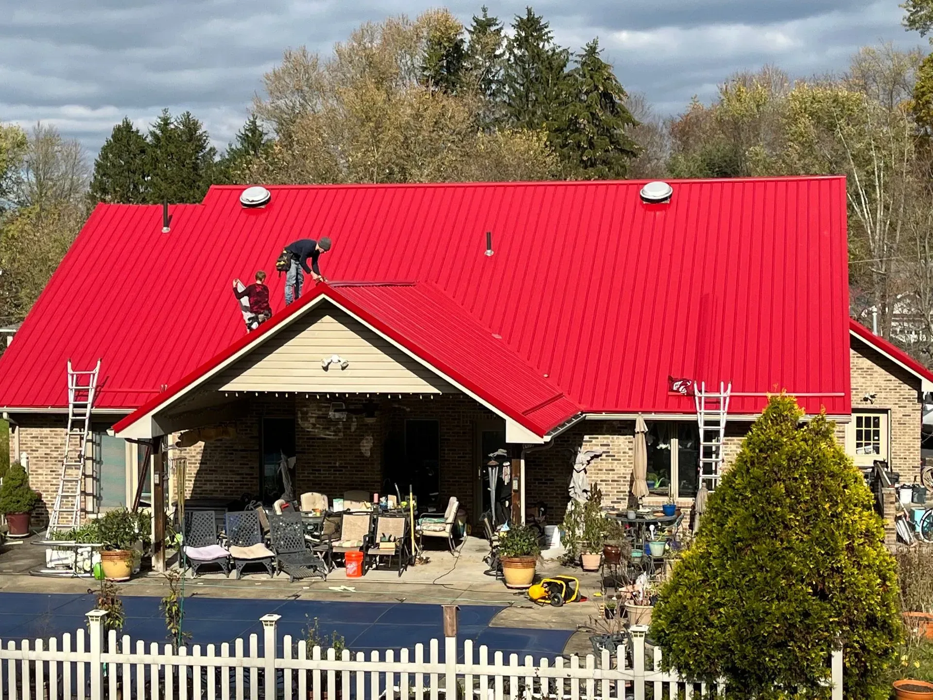 A man is working on the roof of a house with a red roof.