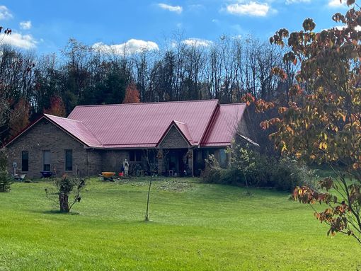 A large house with a red roof is sitting in the middle of a lush green field.